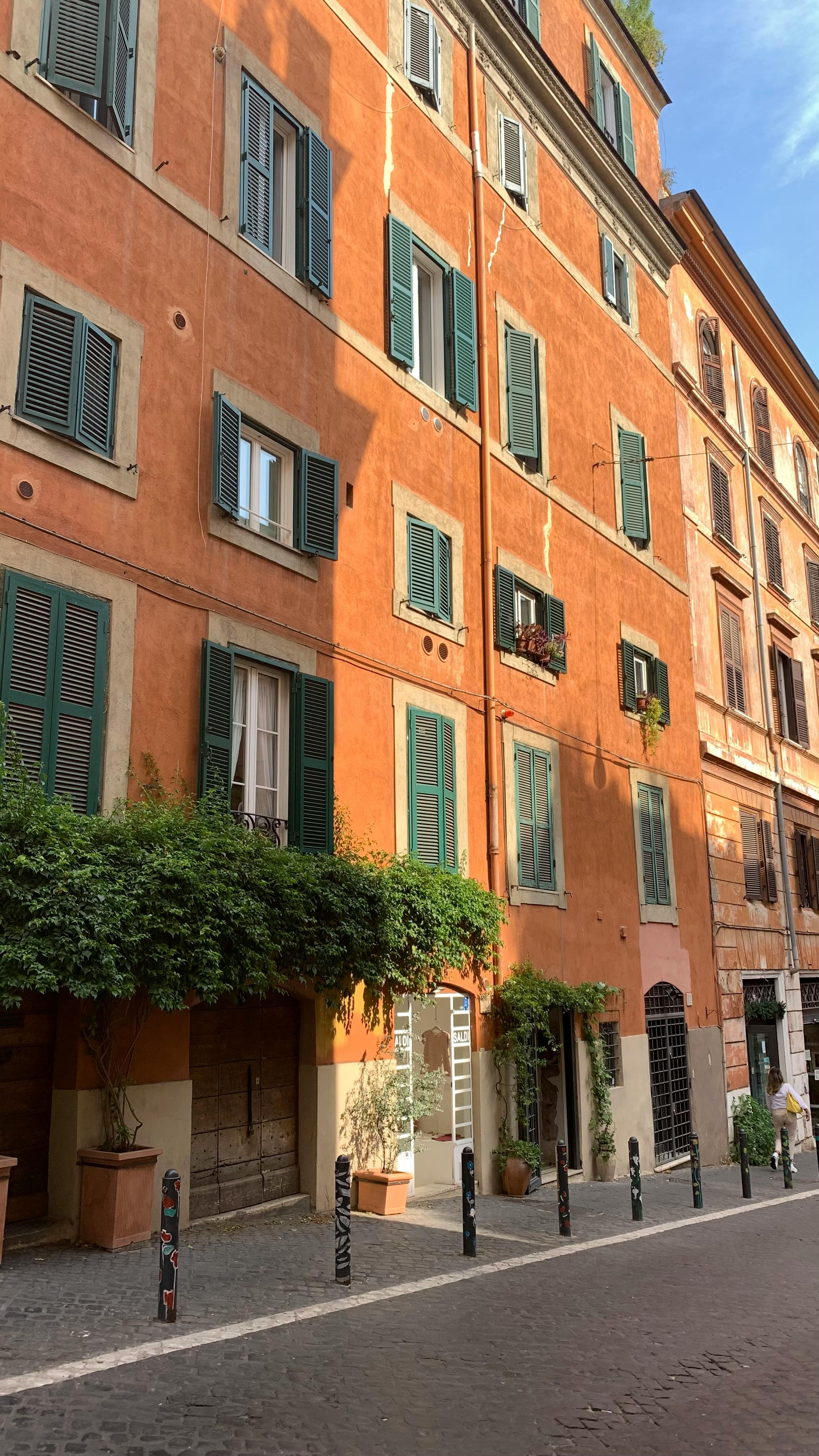 grátis Luz solar quente sobre edifícios romanos históricos com persianas verdes e plantas trepadeiras. Foto profissional