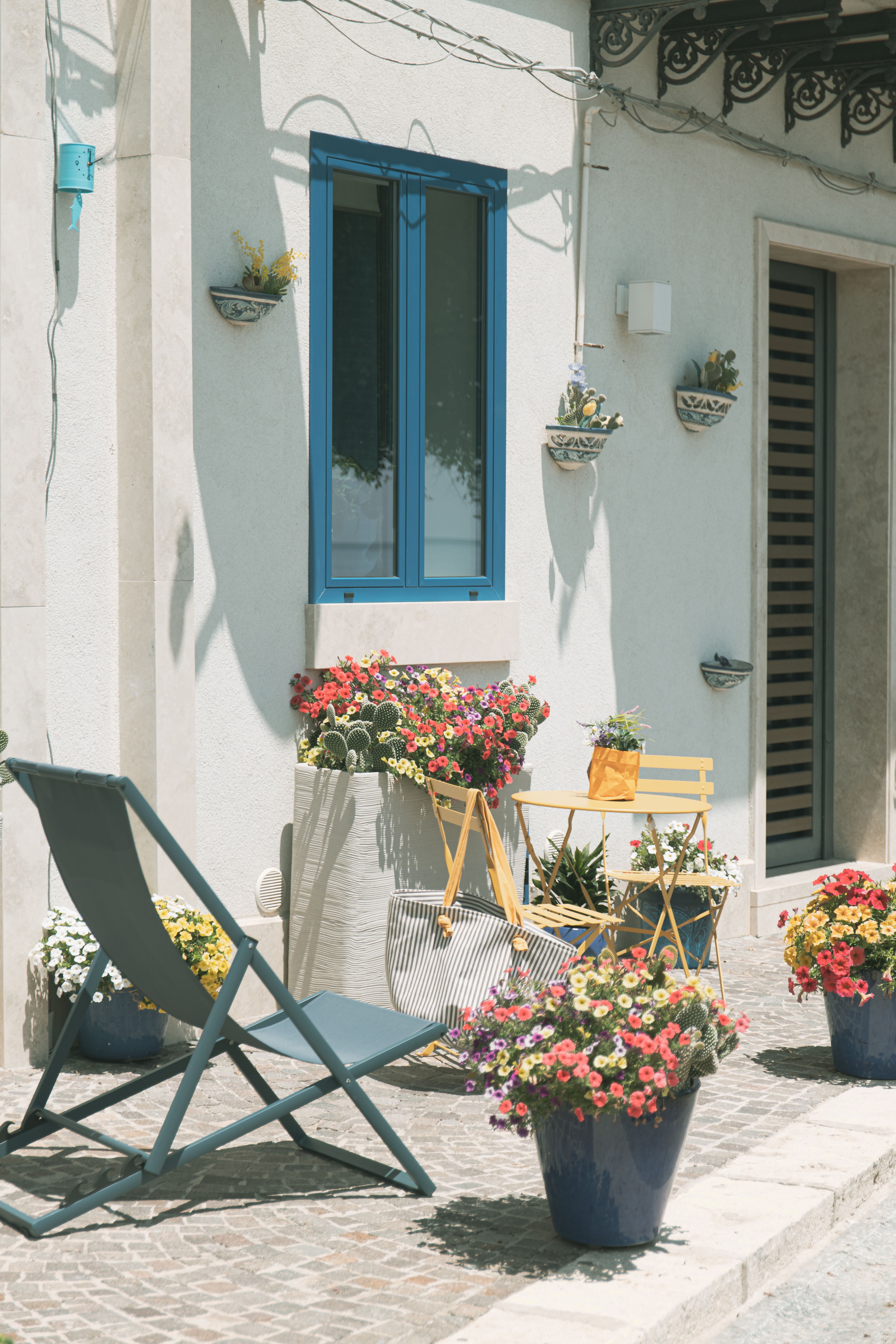 Cozy outdoor patio in Venice with vibrant flowers, blue window details, and seating area.