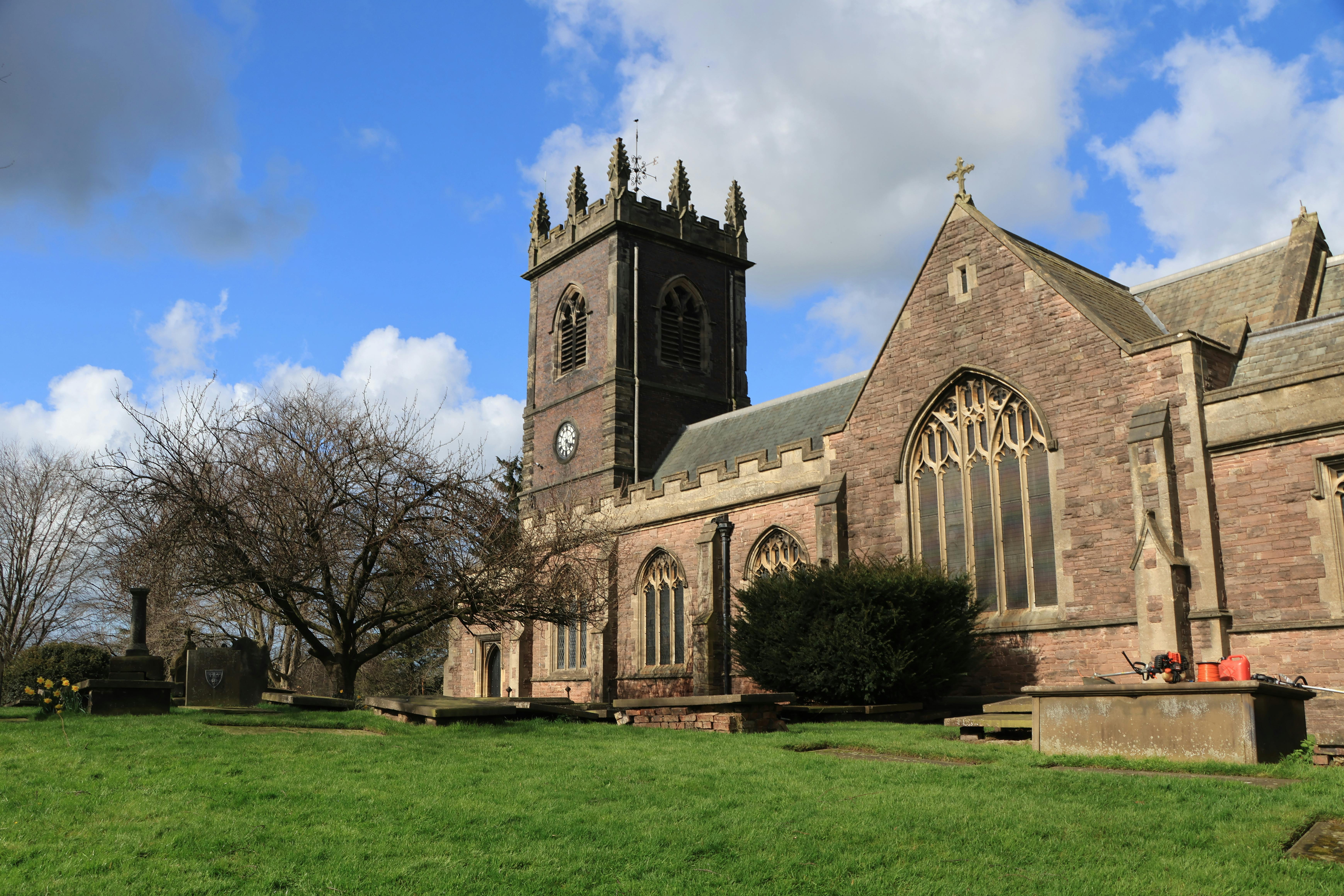 grátis Igreja gótica com torre do relógio em um dia ensolarado, rodeada por árvores e um gramado verde. Foto profissional