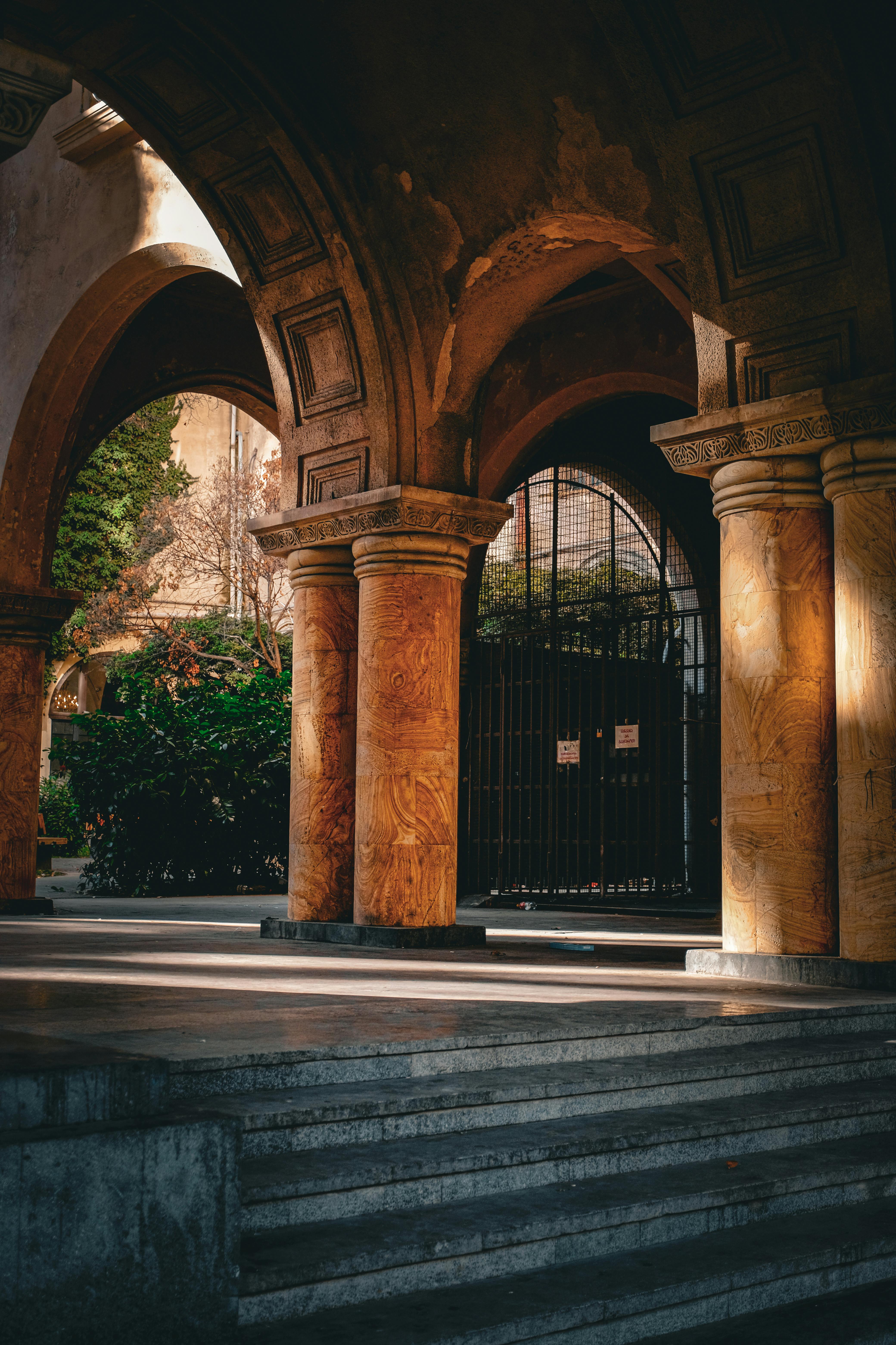 gratis Elegante, zonovergoten bogen en stenen pilaren in een serene binnenplaats in Tbilisi. Stockfoto