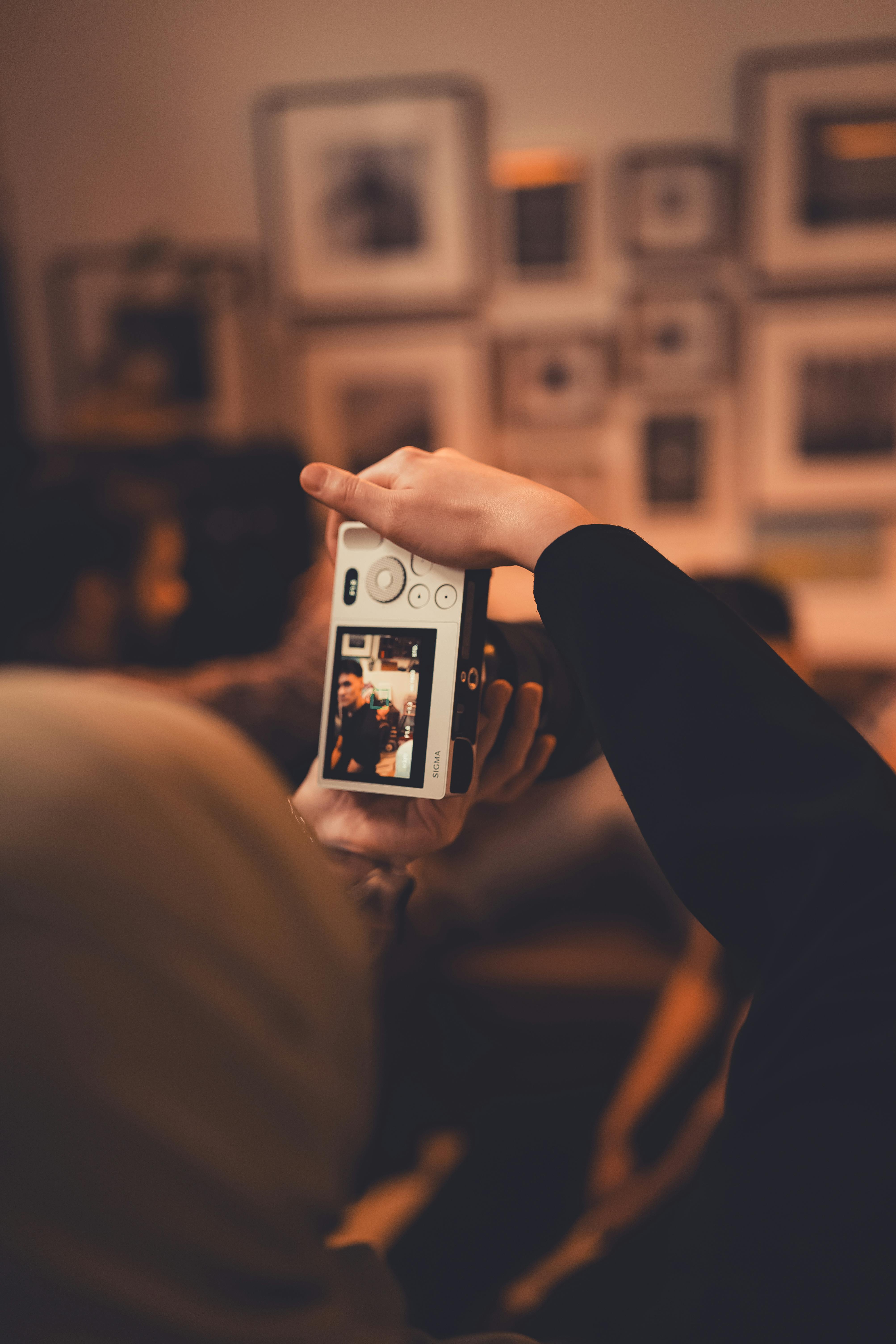 Zadarmo Ruka držiaca vintage fotoaparát zachytávajúci okamih v interiéri s teplým osvetlením, ideálny pre lifestylové témy. Fotka z fotobanky