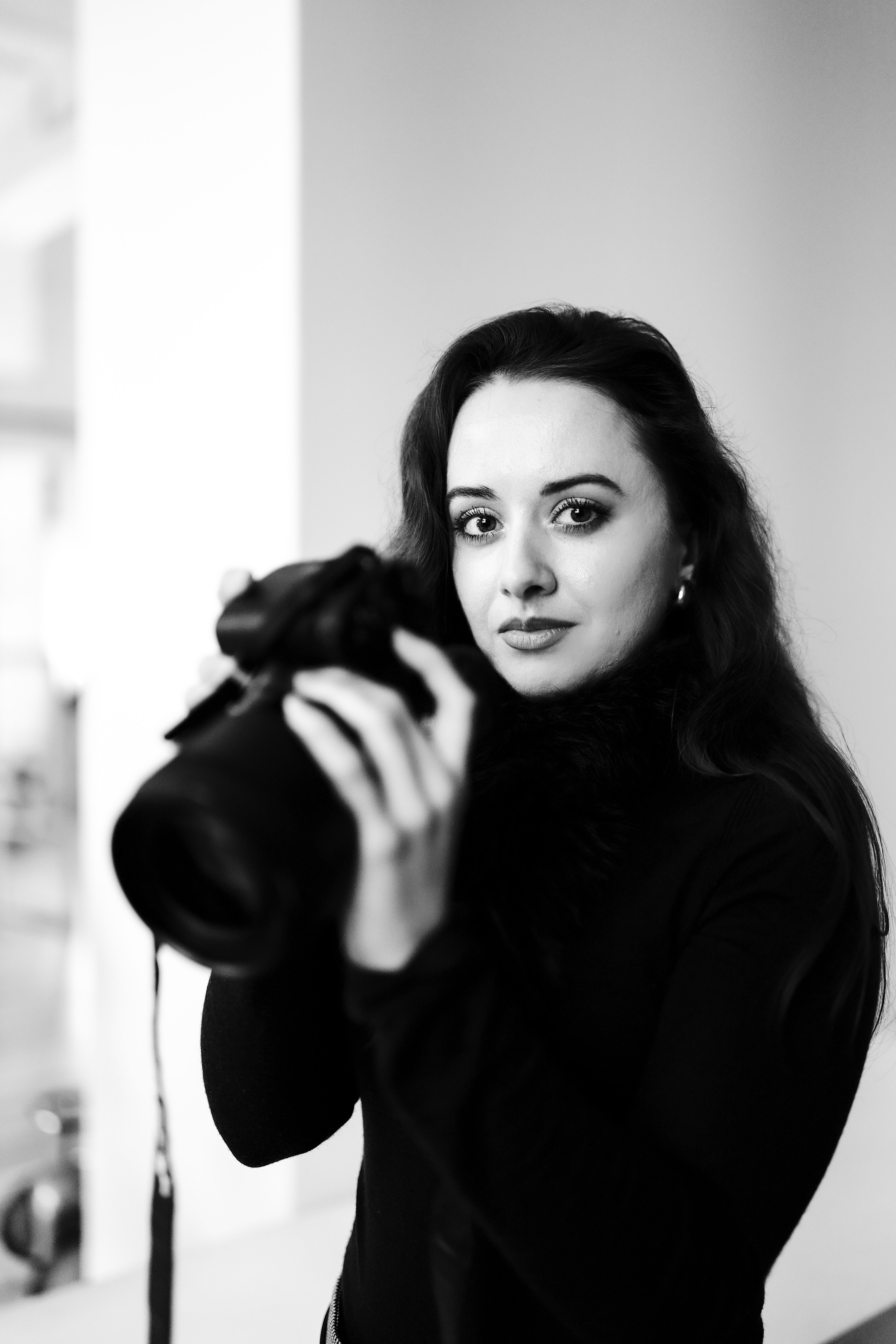 Black and white portrait of a woman photographer holding a camera in a studio.