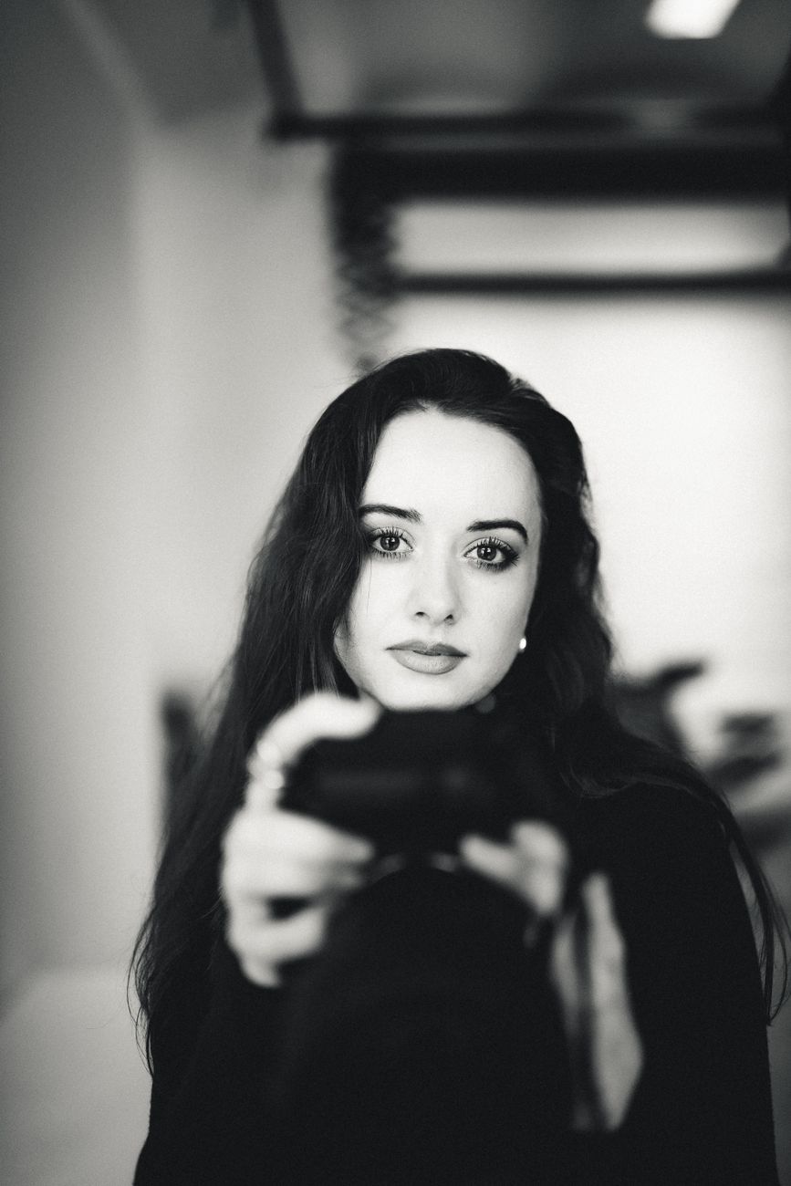 Elegant black and white portrait of a woman holding a camera indoors.
