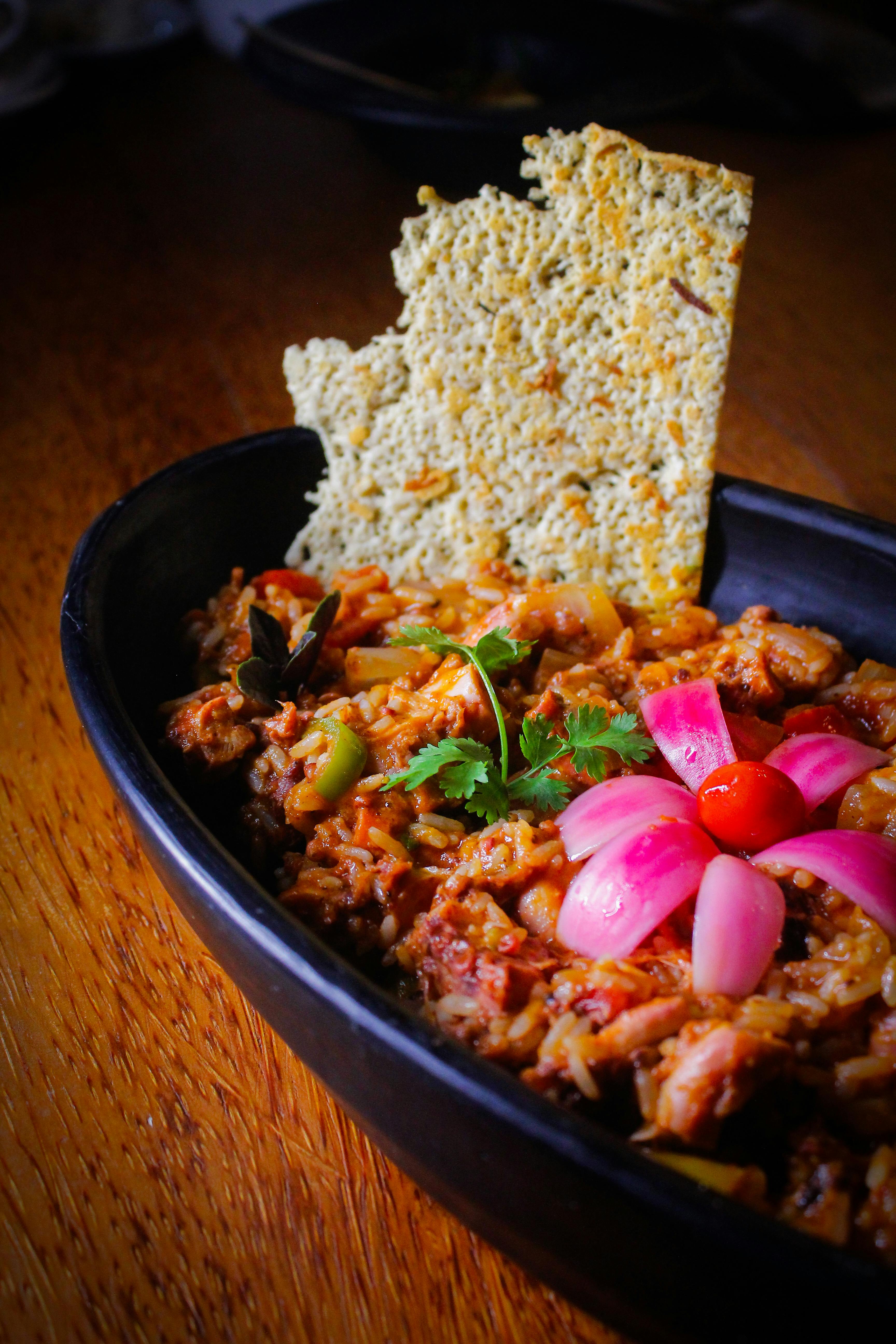 Colorful Indian biryani served with artistic onion flower and papadam in a black dish.