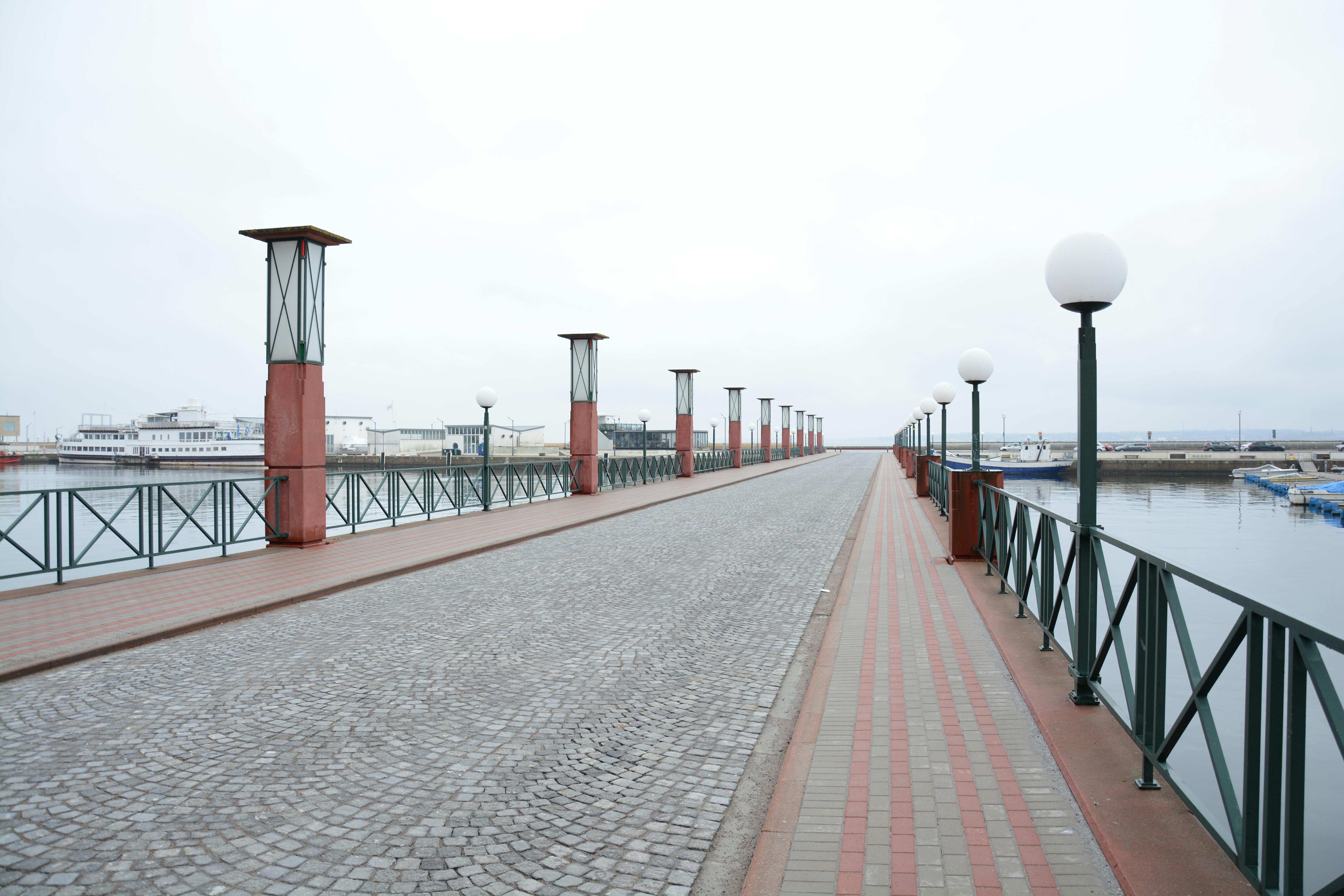 grátis Vista panorâmica de um calçadão deserto à beira-mar em um dia nublado, com postes de iluminação modernos e caminho de paralelepípedos. Foto profissional