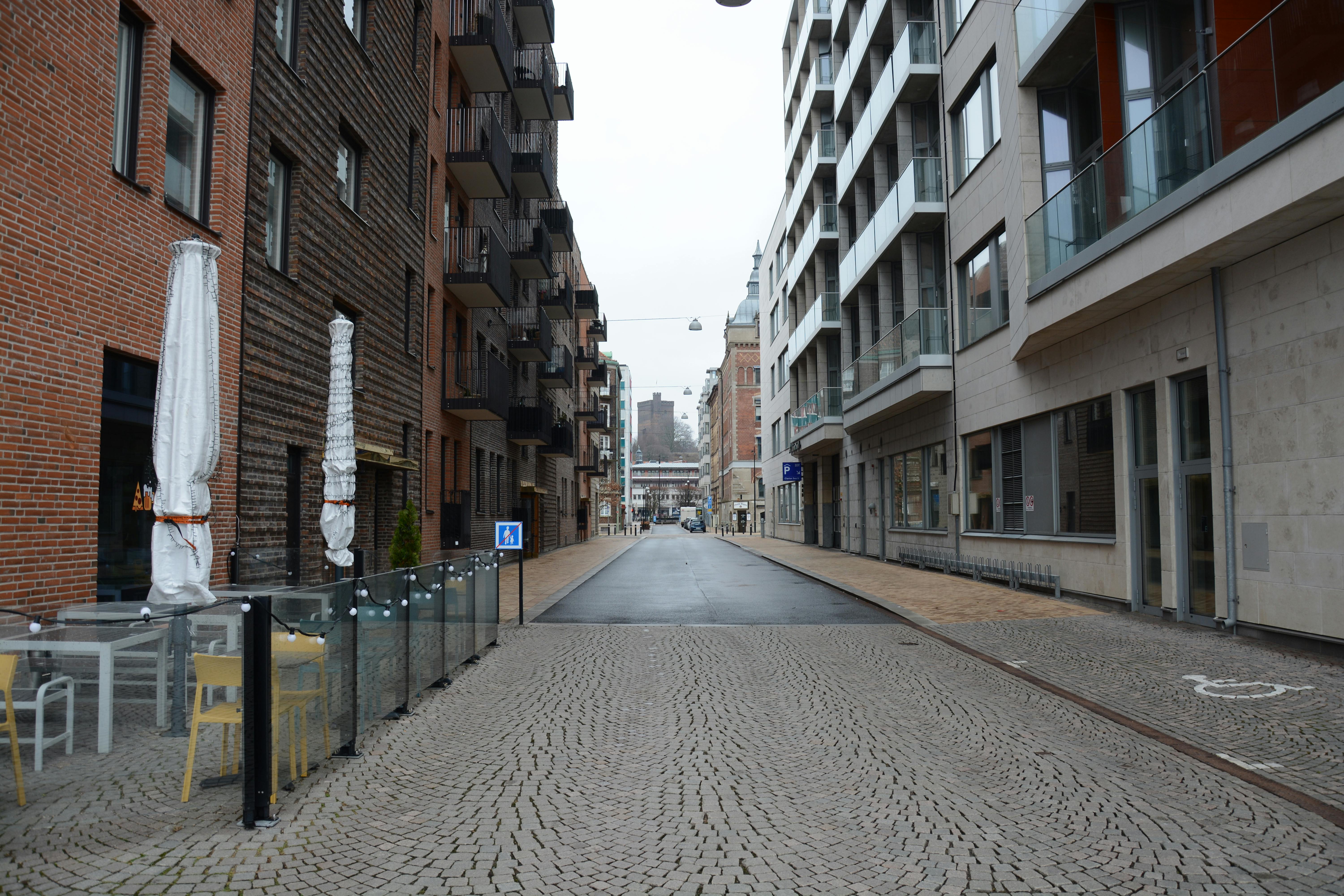 Kostenlos Eine ruhige Kopfsteinpflasterstraße, gesäumt von modernen Wohnungen und Sitzgelegenheiten im Freien in urbanem Umfeld. Stock-Foto
