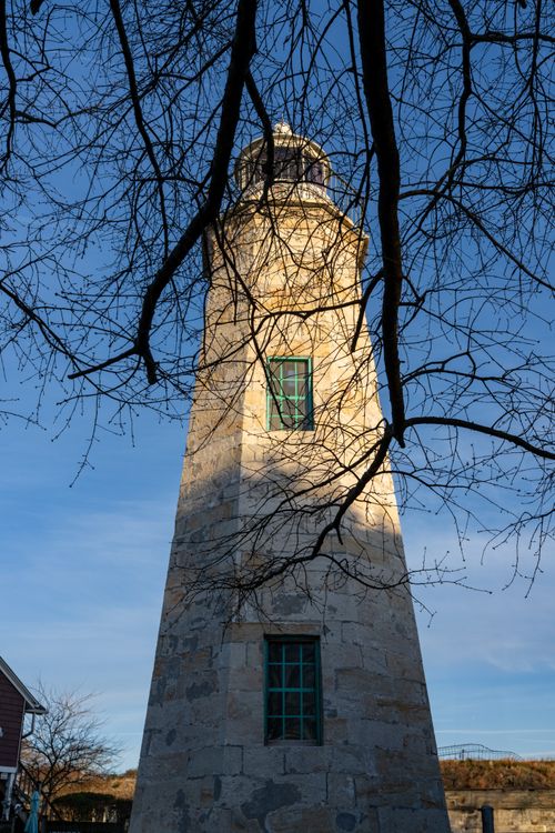 Free A picturesque view of a historic lighthouse framed by bare branches in Hampton, Virginia. Stock Photo