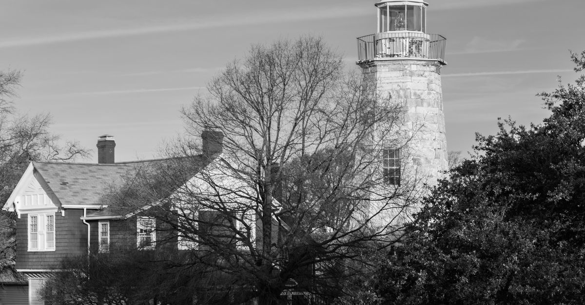 Black and white photo of a historic lighthouse and house surrounded by trees in Hampton, Virginia.