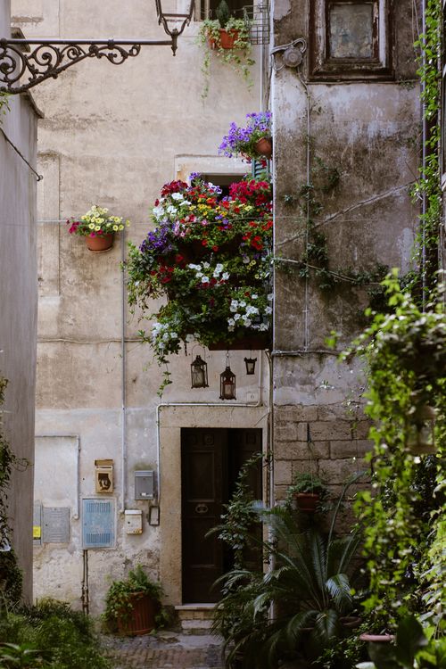 Free Explore a picturesque Italian alley adorned with vibrant flowers cascading from a rustic balcony. Stock Photo