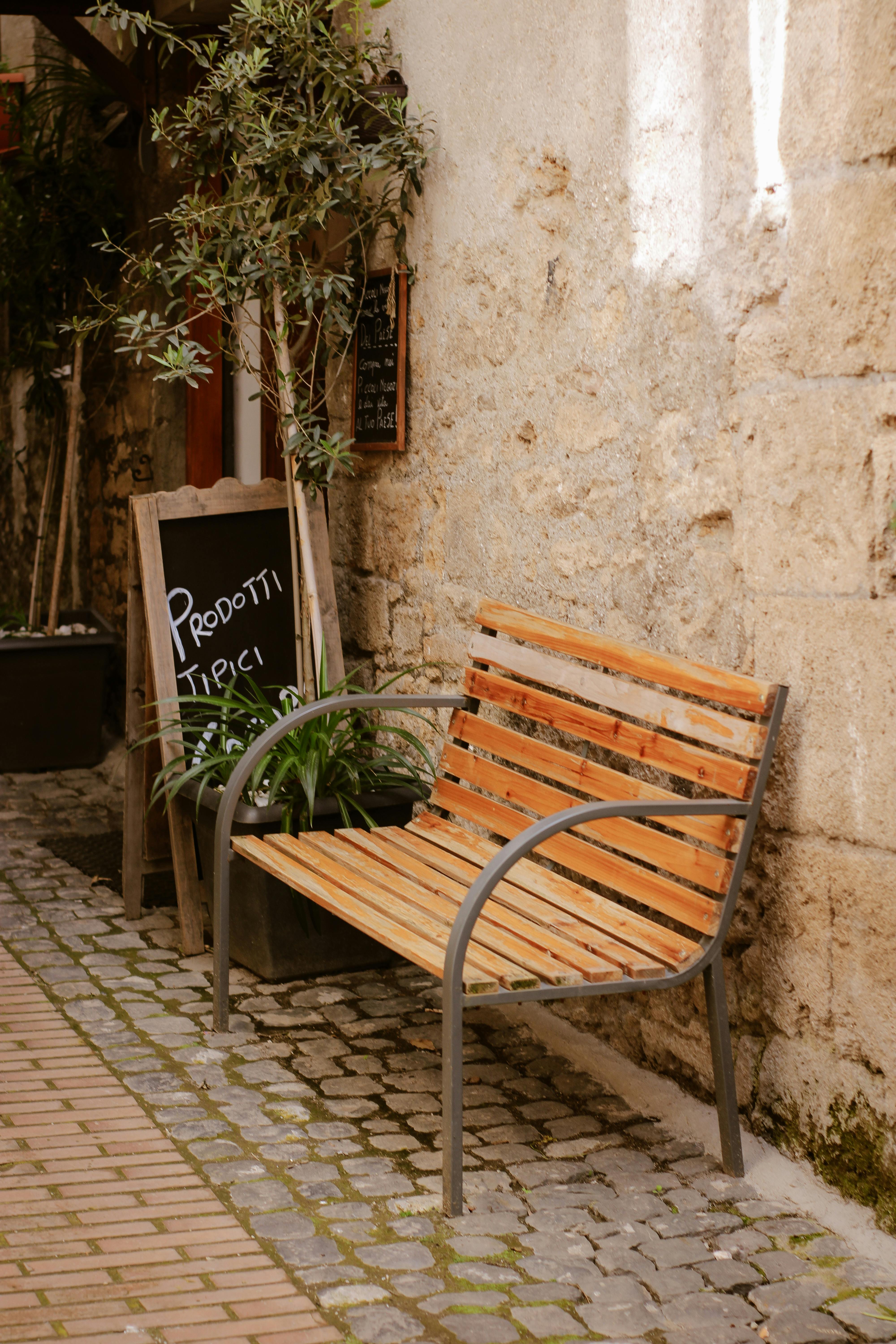 ฟรี ตรอกเล็กๆ ที่อบอุ่นในอิตาลี มีม้านั่งไม้และป้ายกระดานดำแนะนำสินค้าท้องถิ่น คลังภาพถ่าย