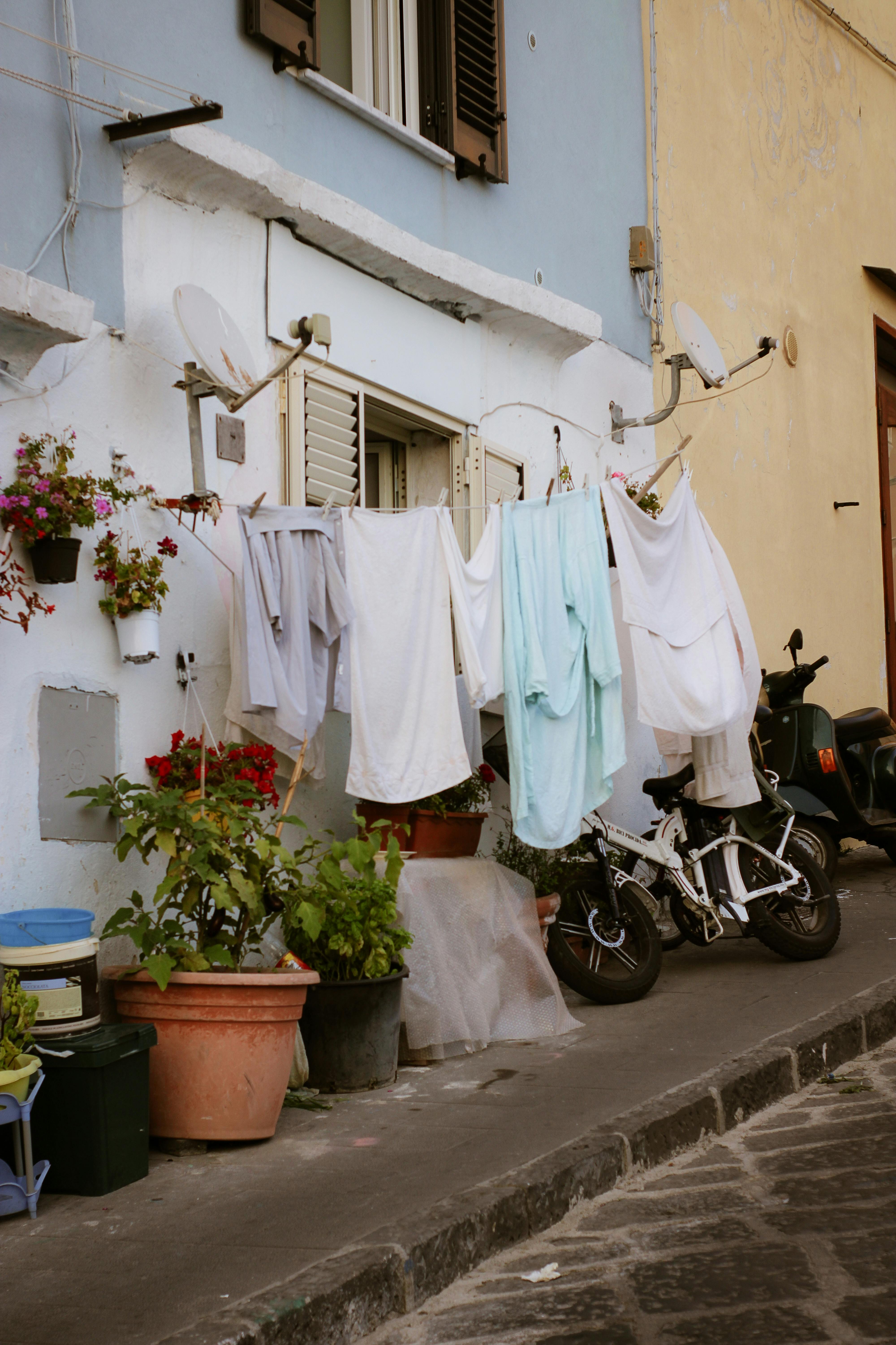 ฟรี ภาพบรรยากาศถนนในอิตาลีที่ดูแปลกตา พร้อมผ้าสีสันสดใสที่แขวนอยู่บนผนังอาคารสไตล์ชนบท คลังภาพถ่าย