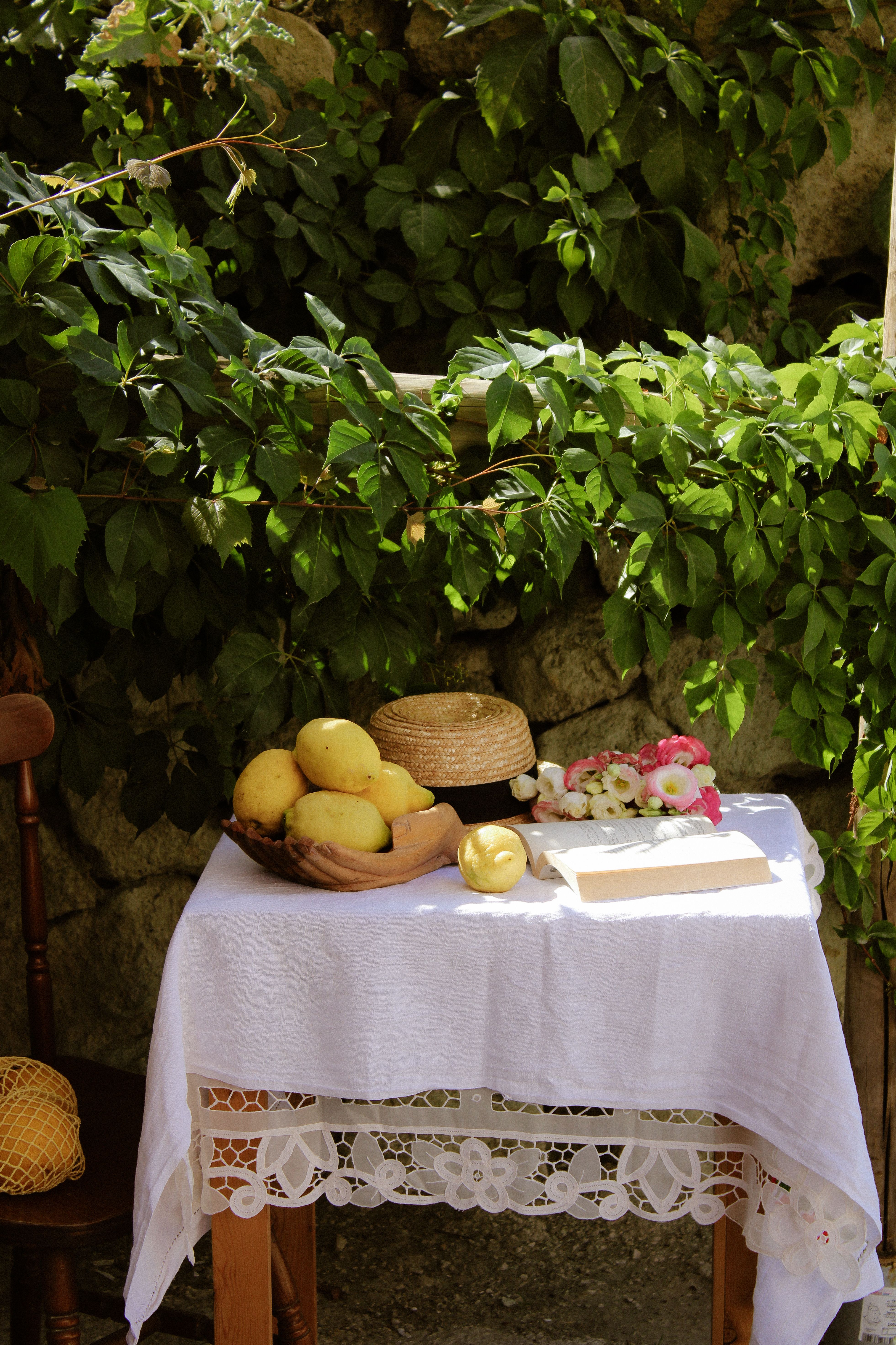 Serene outdoor still life with lemons and hat under lush foliage in Italy.
