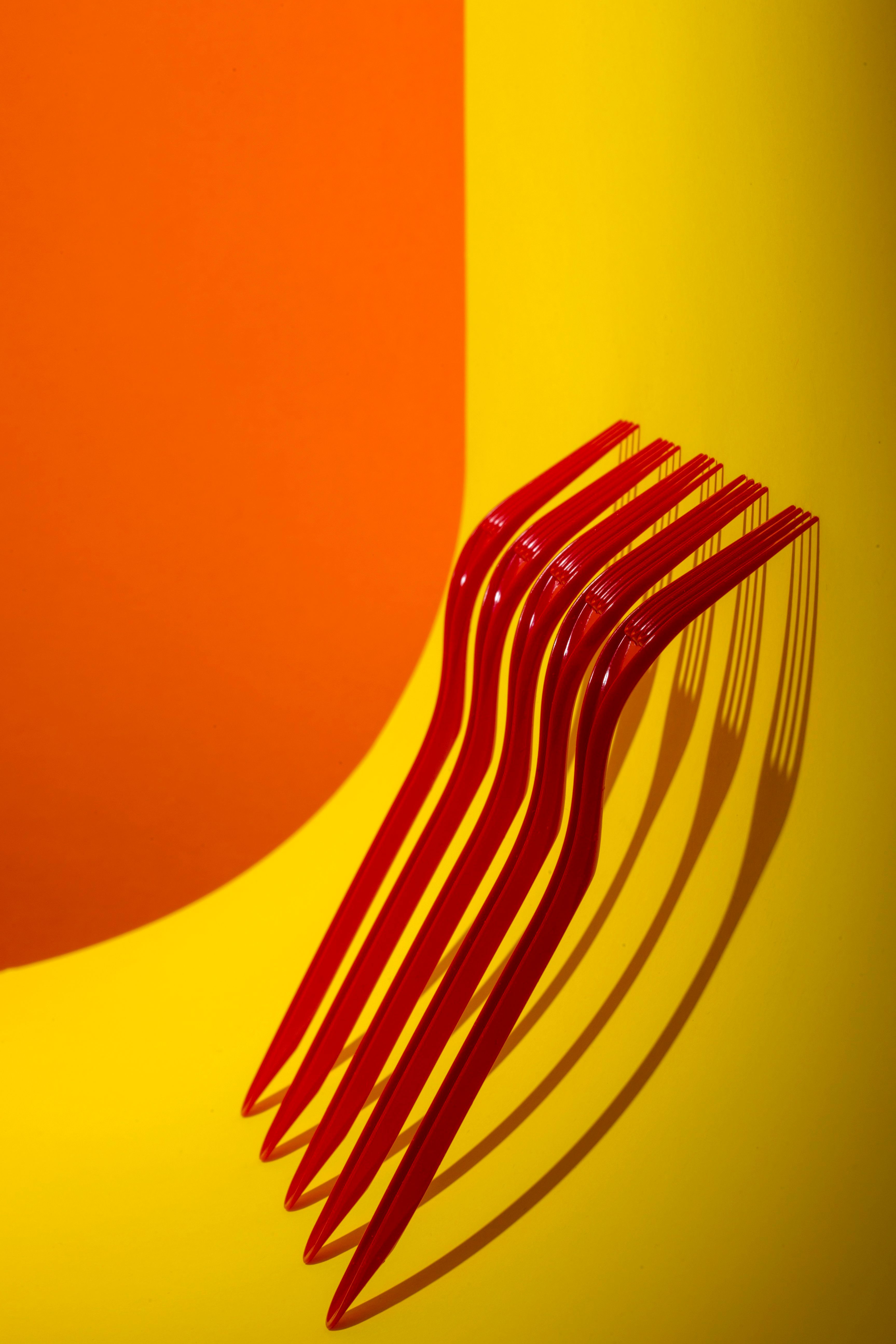 Artistic composition of red forks casting shadows on a vivid orange and yellow backdrop.