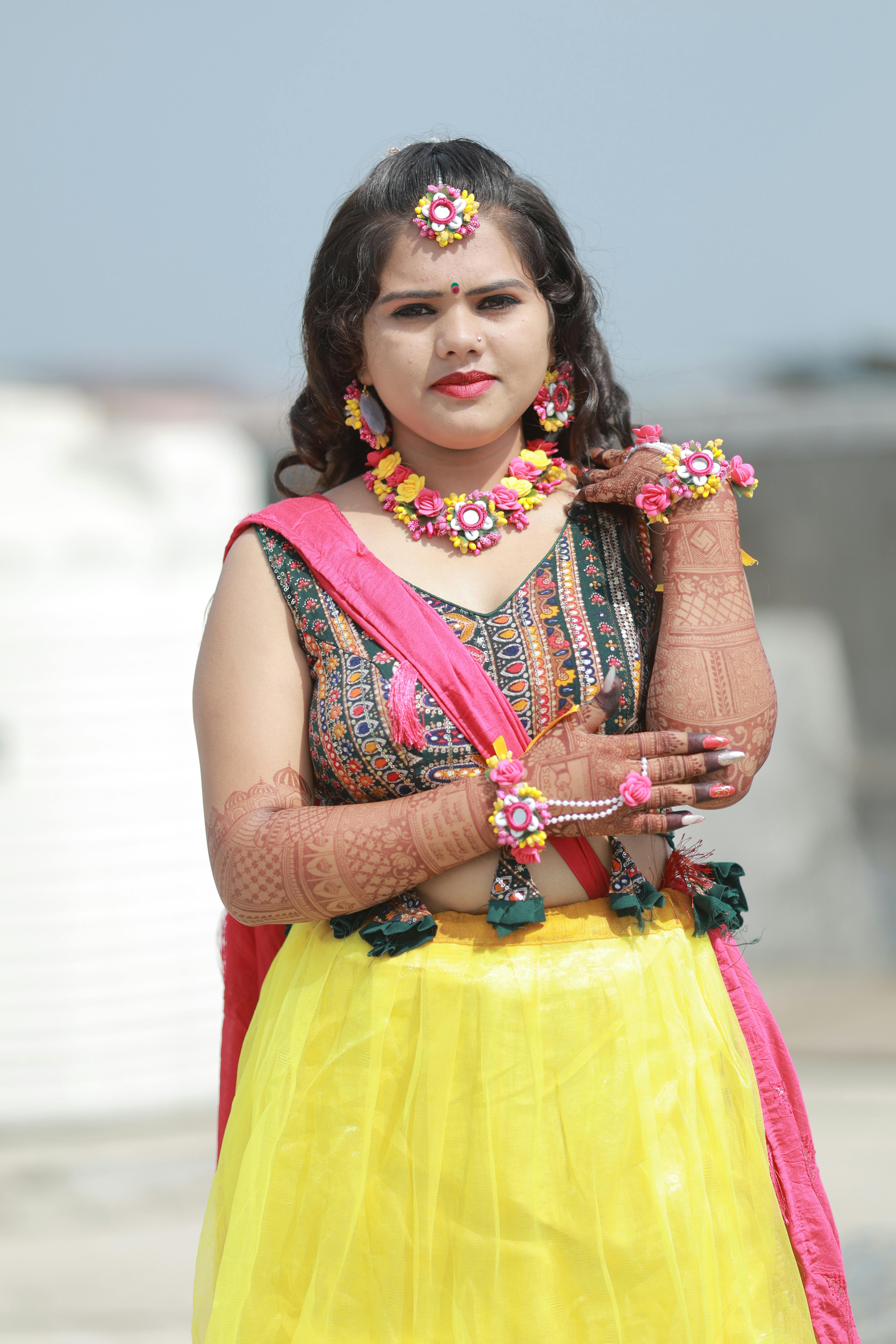 Gratis En kvinne i tradisjonell antrekk med blomstersmykker poserer for en bryllupsfotografering utendørs. Arkivbilde