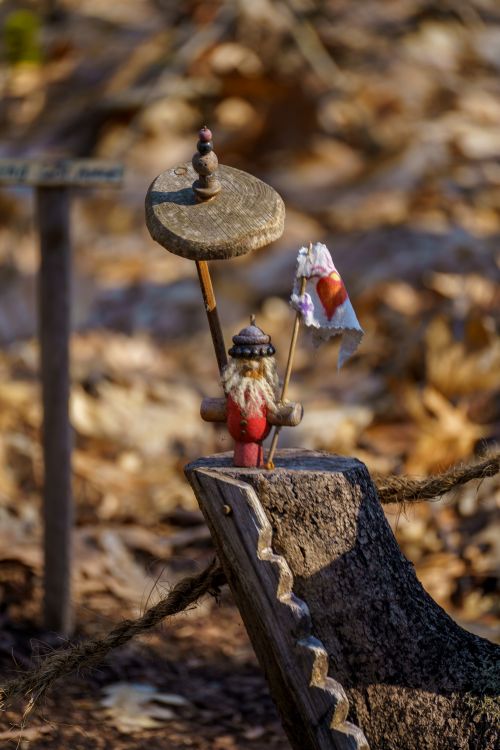 Free Charming gnome statue holding an umbrella and heart flag, surrounded by autumn leaves in a forest. Stock Photo