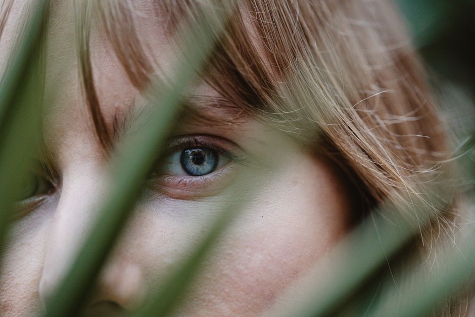 A close-up shot of a blue eye partially hidden behind green leaves.