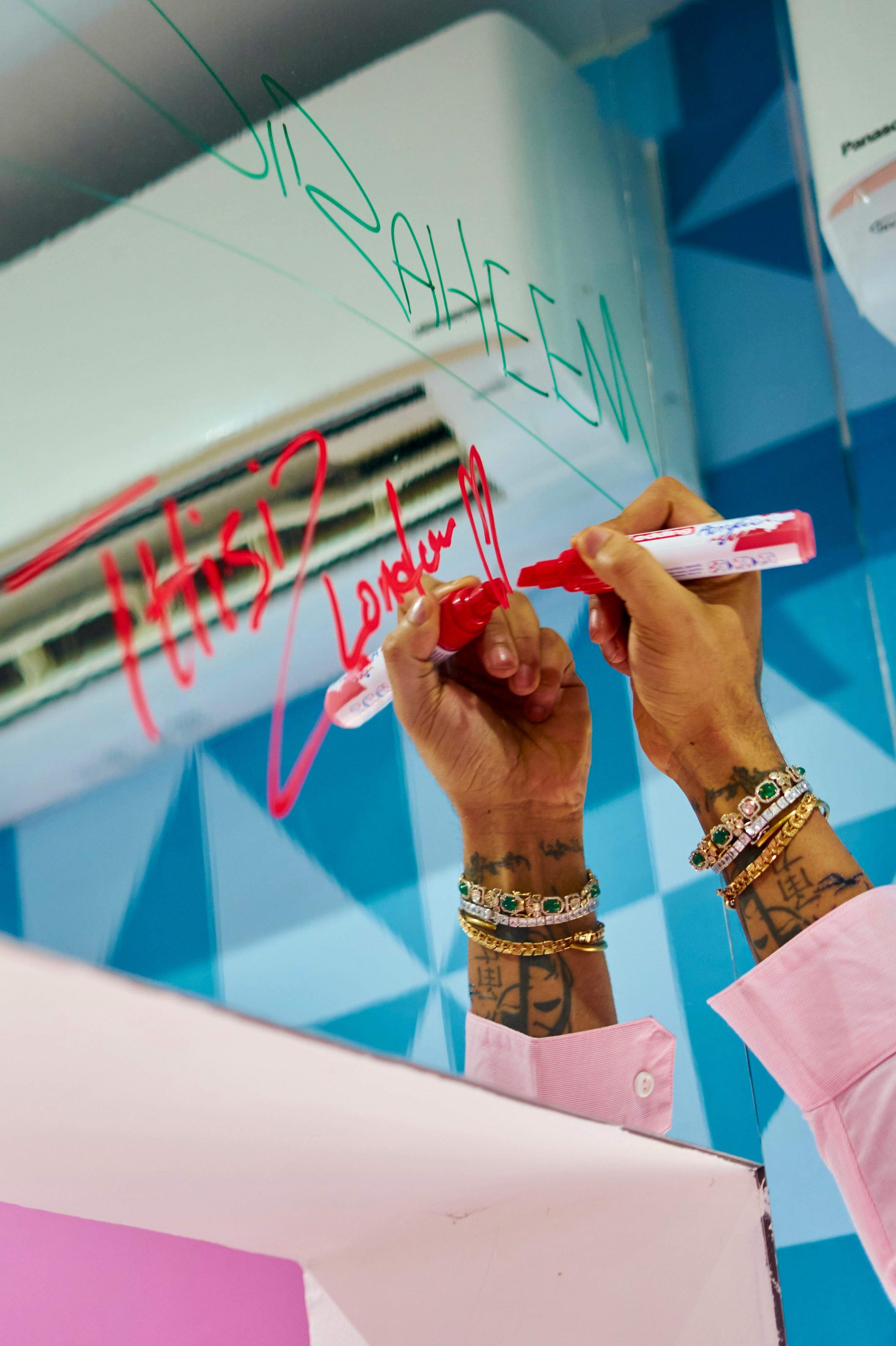 ฟรี ภาพห้องน้ำสีสันสดใส มีคนกำลังเขียนบนกระจกด้วยปากกาเมจิก และเห็นกำไลข้อมือเก๋ๆ อยู่ด้วย คลังภาพถ่าย