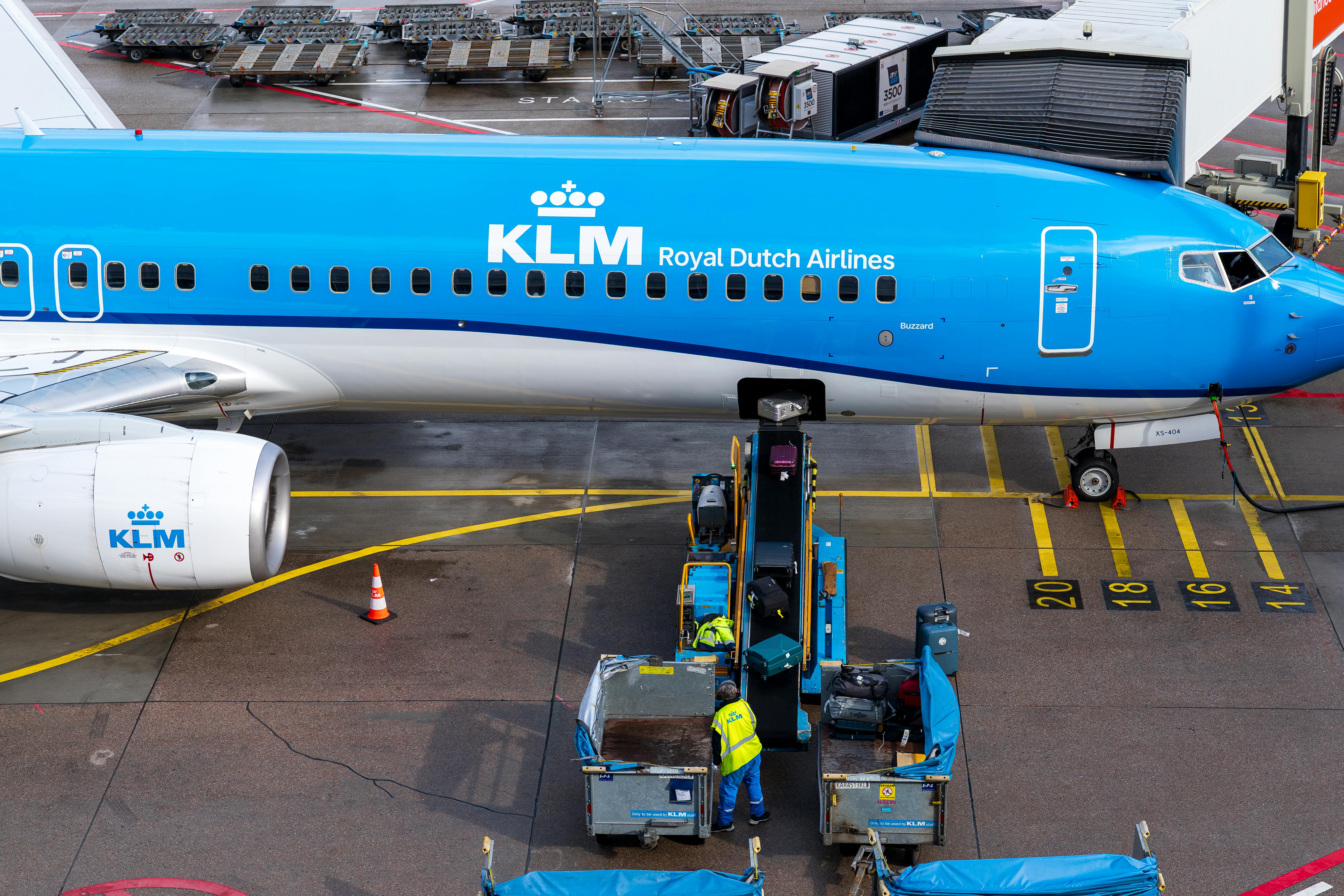 bezplatná Letadlo KLM je nakládáno u terminálu zavazadlovými vozíky a dělníci se připravují na let. Základová fotografie