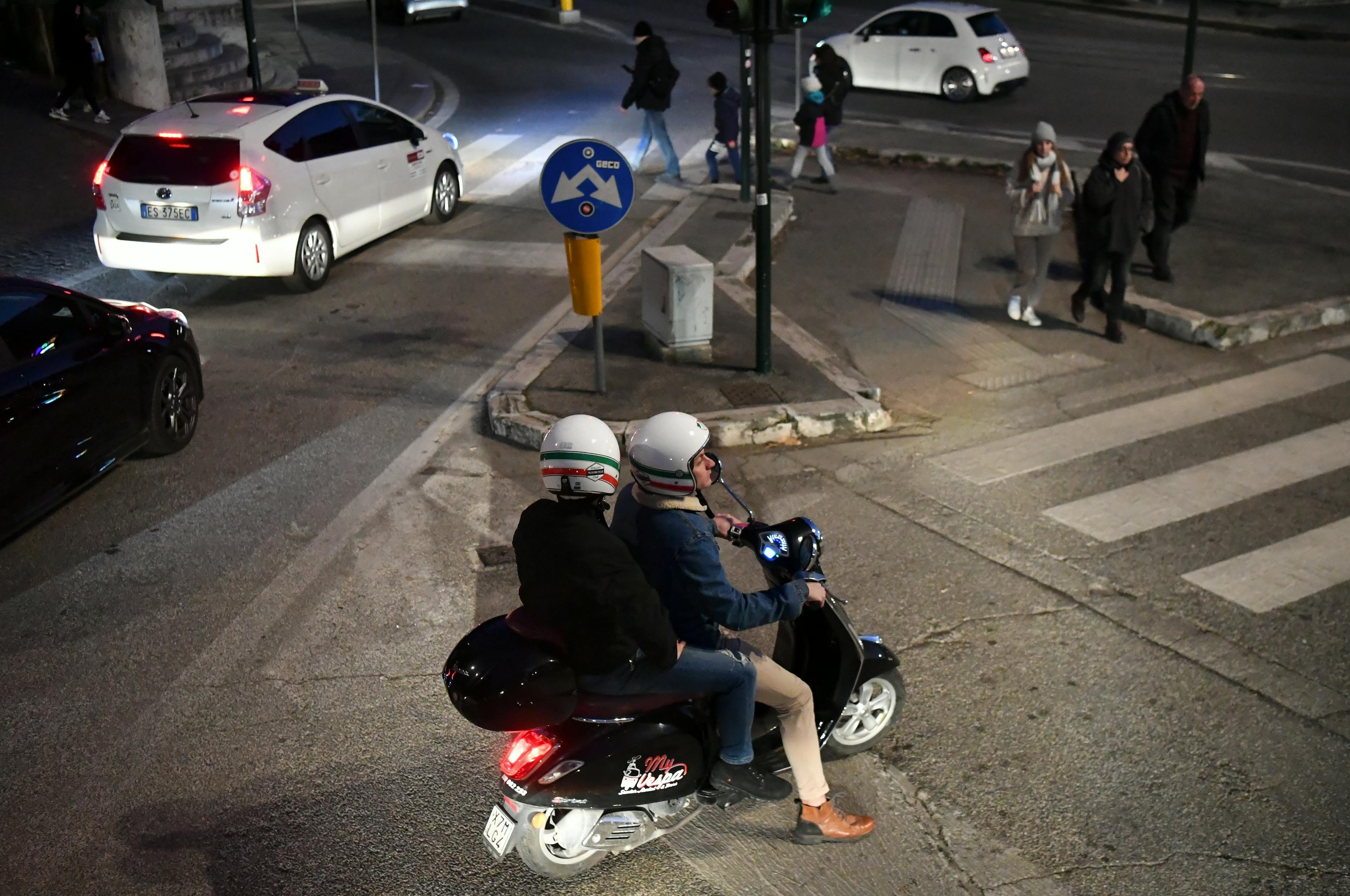 무료 밤에 도시의 횡단보도에서 스쿠터를 탄 두 사람이 기다리고 있다. 스톡 사진
