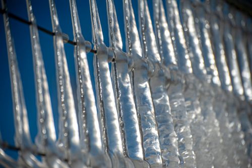Free Detailed view of icicles hanging on a fence reflecting sunlight against a clear blue sky. Stock Photo