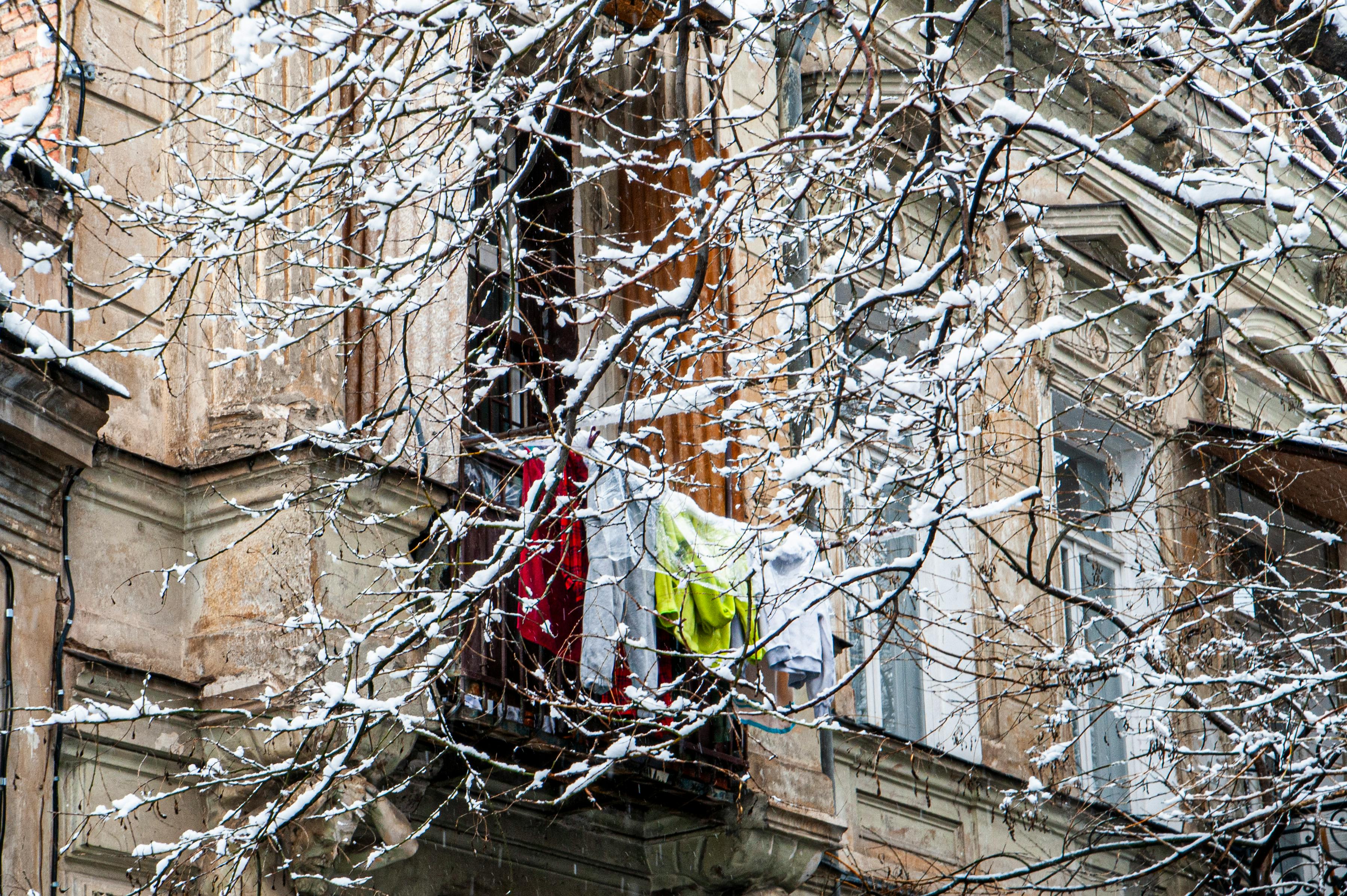 免费 第比利斯一座历史悠久的阳台上晾晒着衣服，与白雪皑皑的城市背景形成鲜明对比。 素材图片