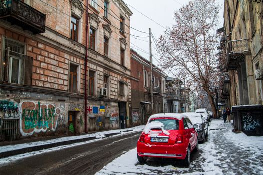 A snowy street with cars and graffiti-covered buildings in Tbilisi, Georgia.