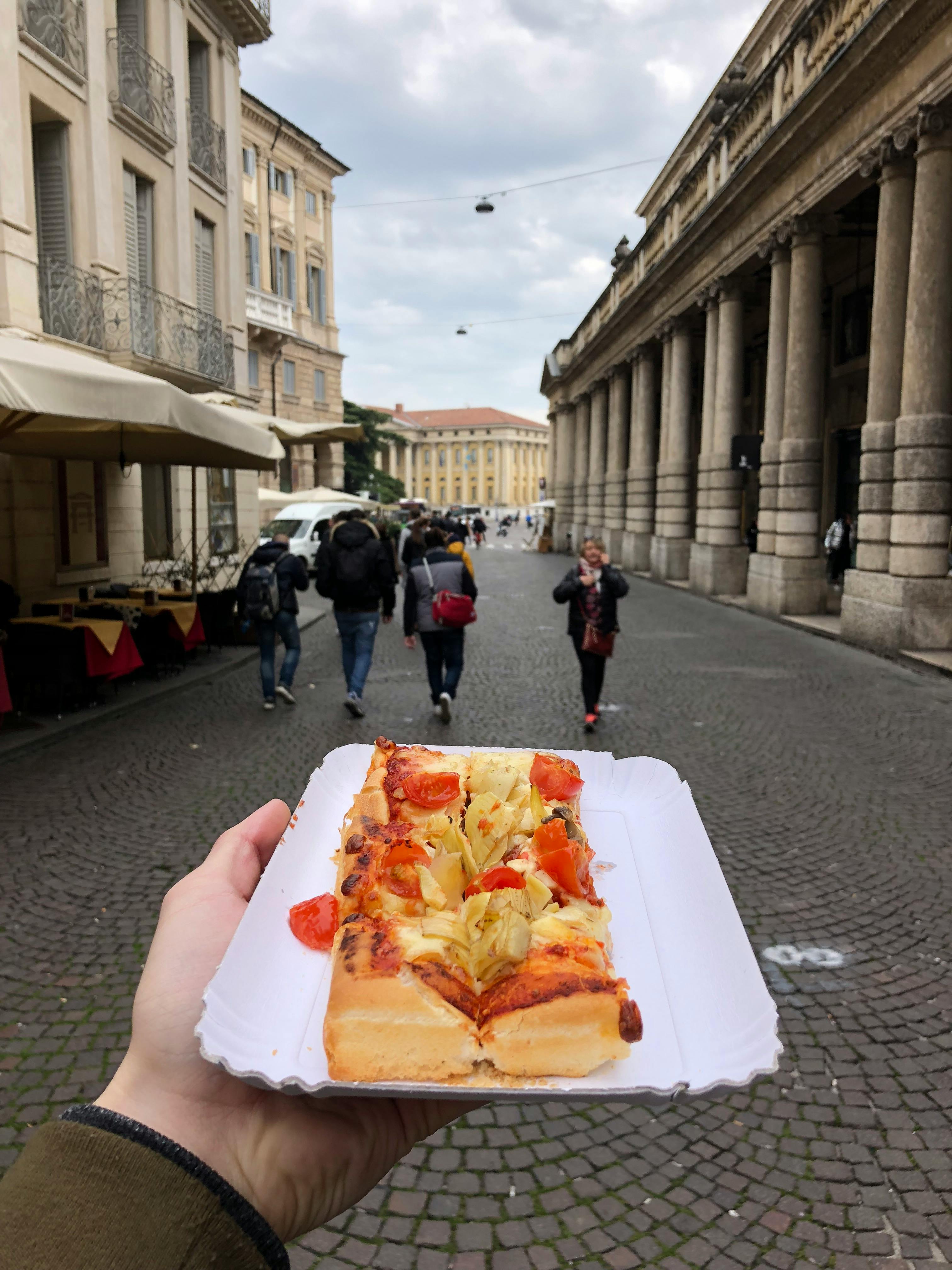 De franc Gaudint d'un tros de pizza deliciosa en un carrer bulliciós de Verona, Itàlia. Foto d'estoc