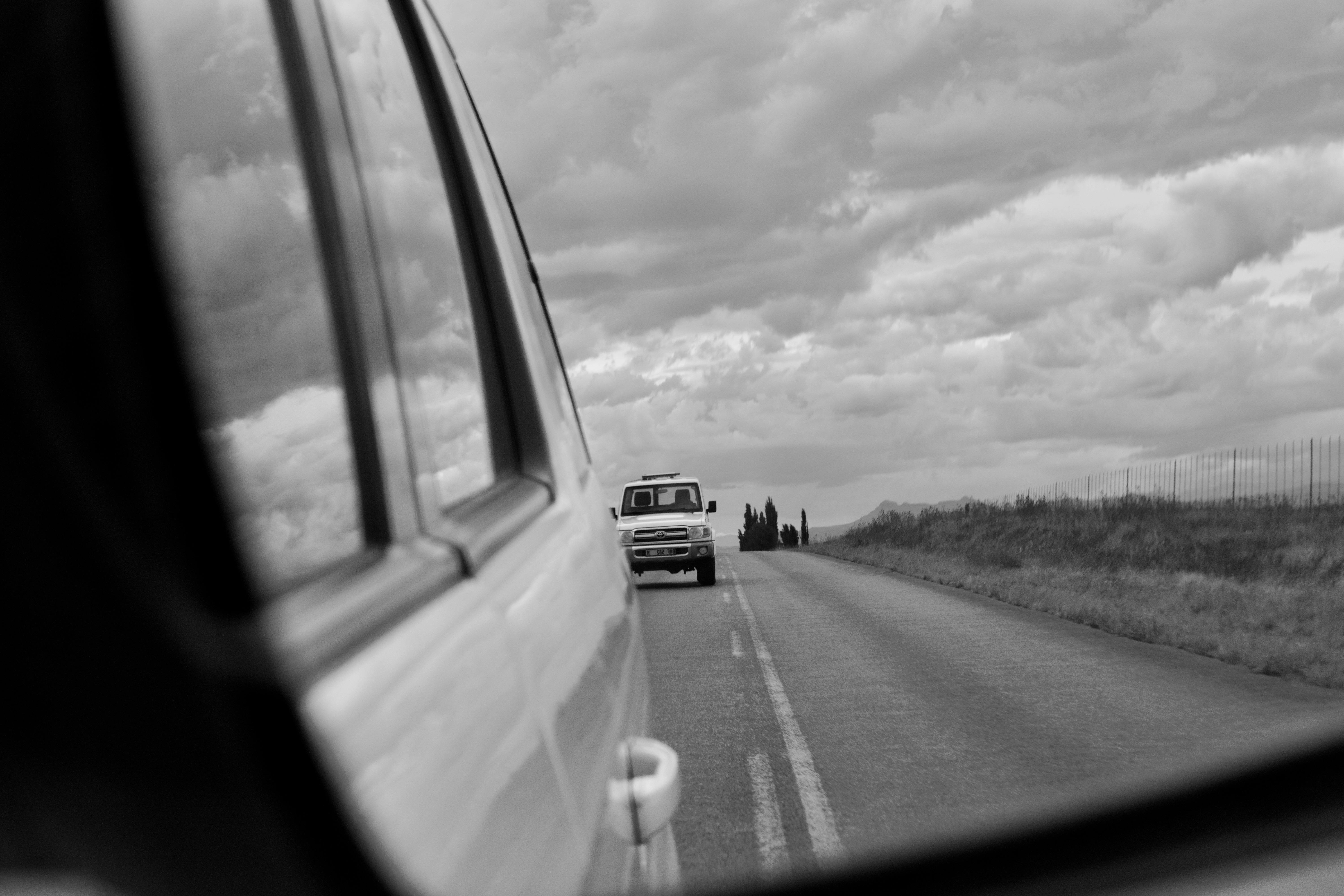 Безкоштовне Монохромне зображення автомобіля, що видно через бічне дзеркало на сільській дорозі. стокове фото