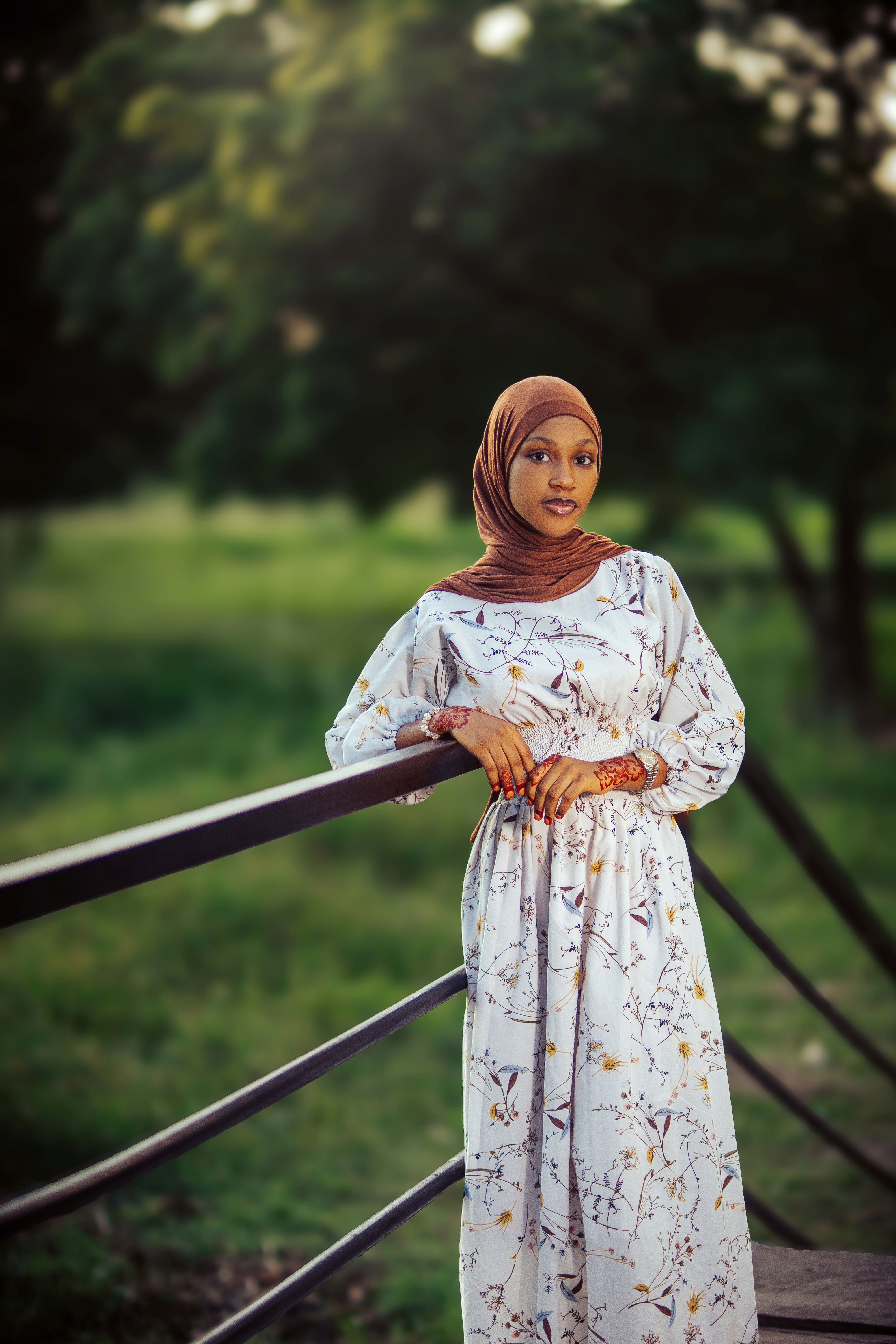 A portrait of a young woman wearing a hijab, standing by a railing outdoors in Nigeria.