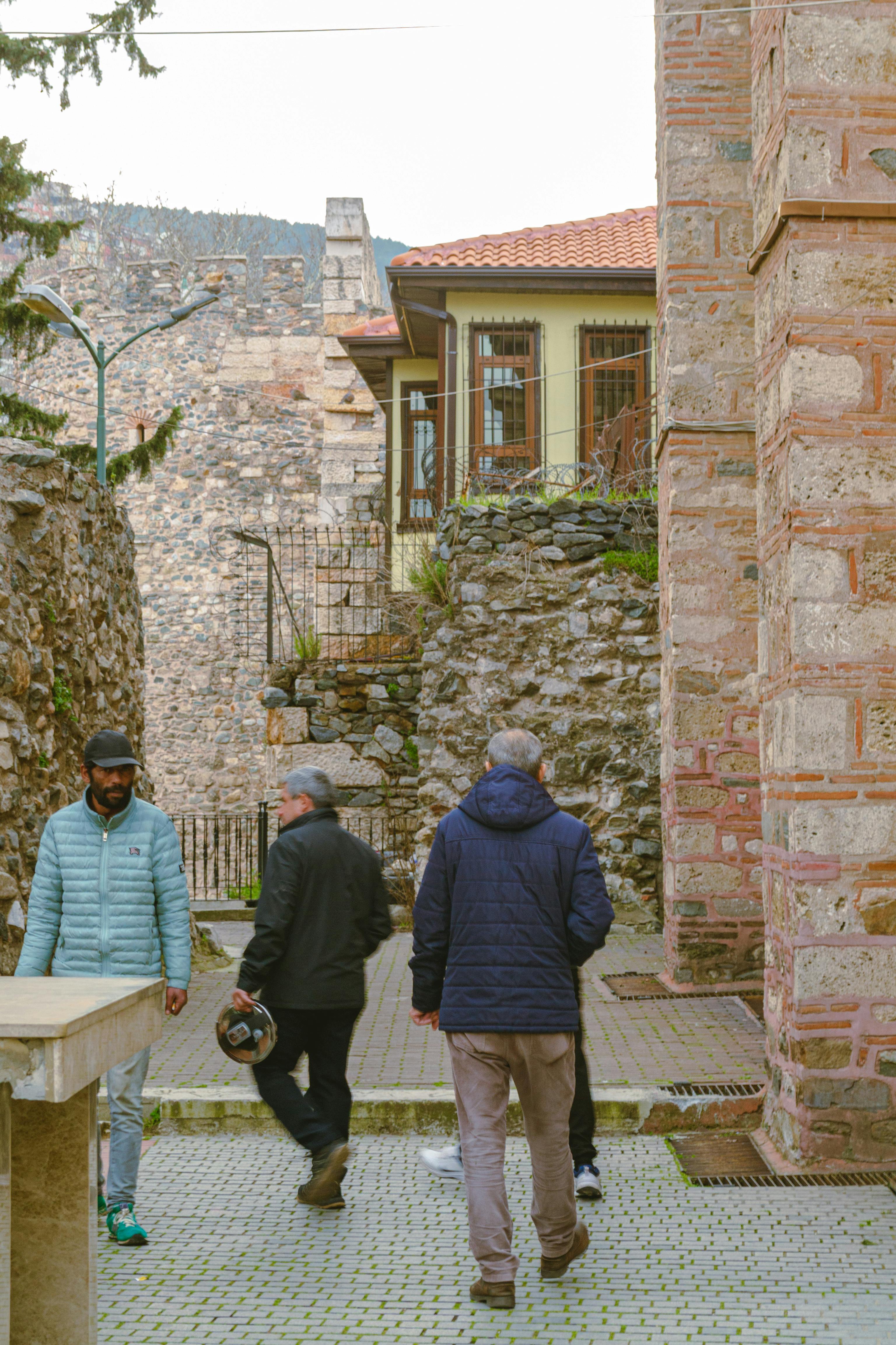 ฟรี คนสามคนกำลังเดินเล่นในตรอกหินเก่าแก่ ที่แสดงให้เห็นถึงสถาปัตยกรรมโบราณและวิถีชีวิตในเมืองที่เรียบง่าย คลังภาพถ่าย