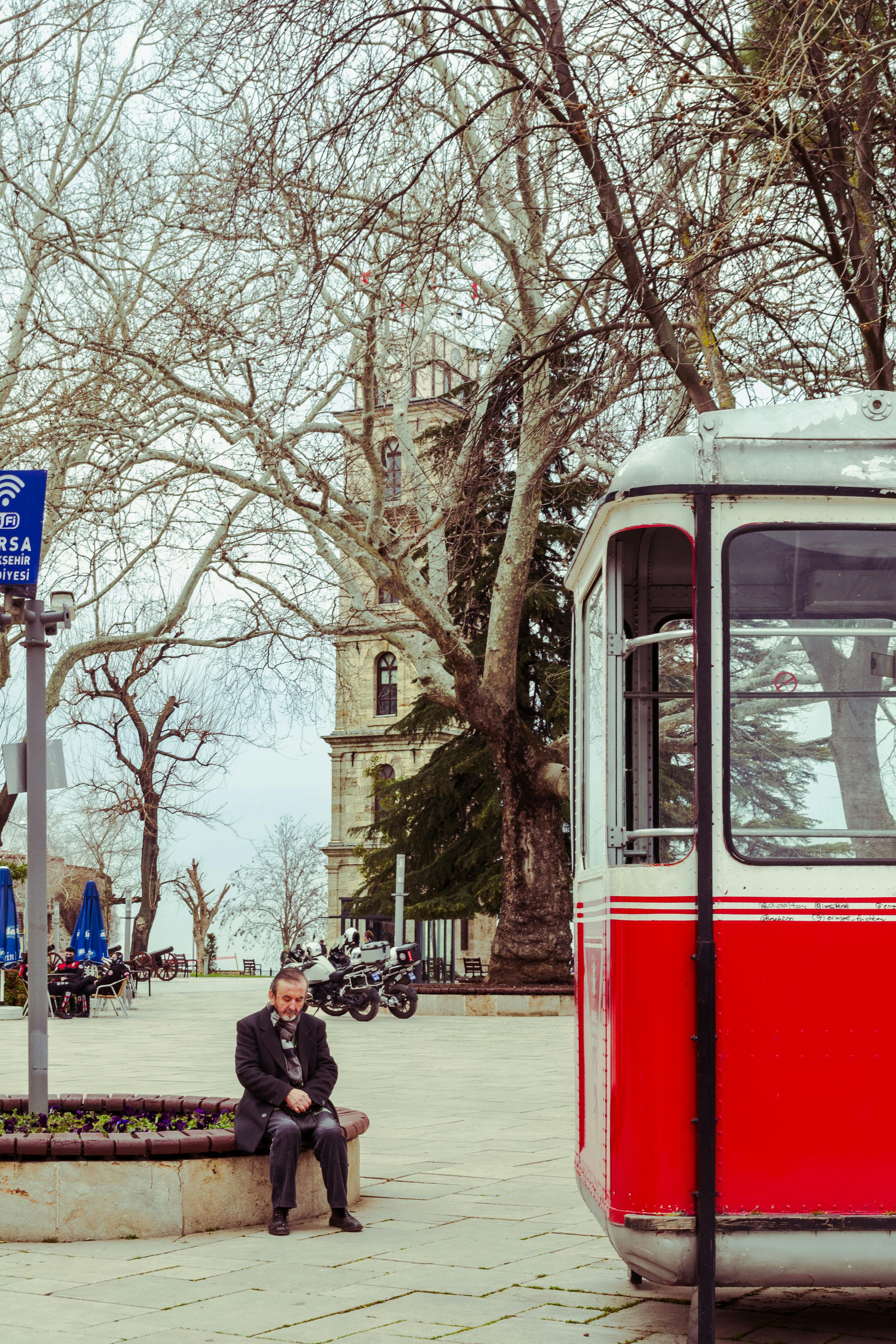 Zadarmo Scéna v parku s červenou električkou, listnatými stromami a historickou budovou. Fotka z fotobanky