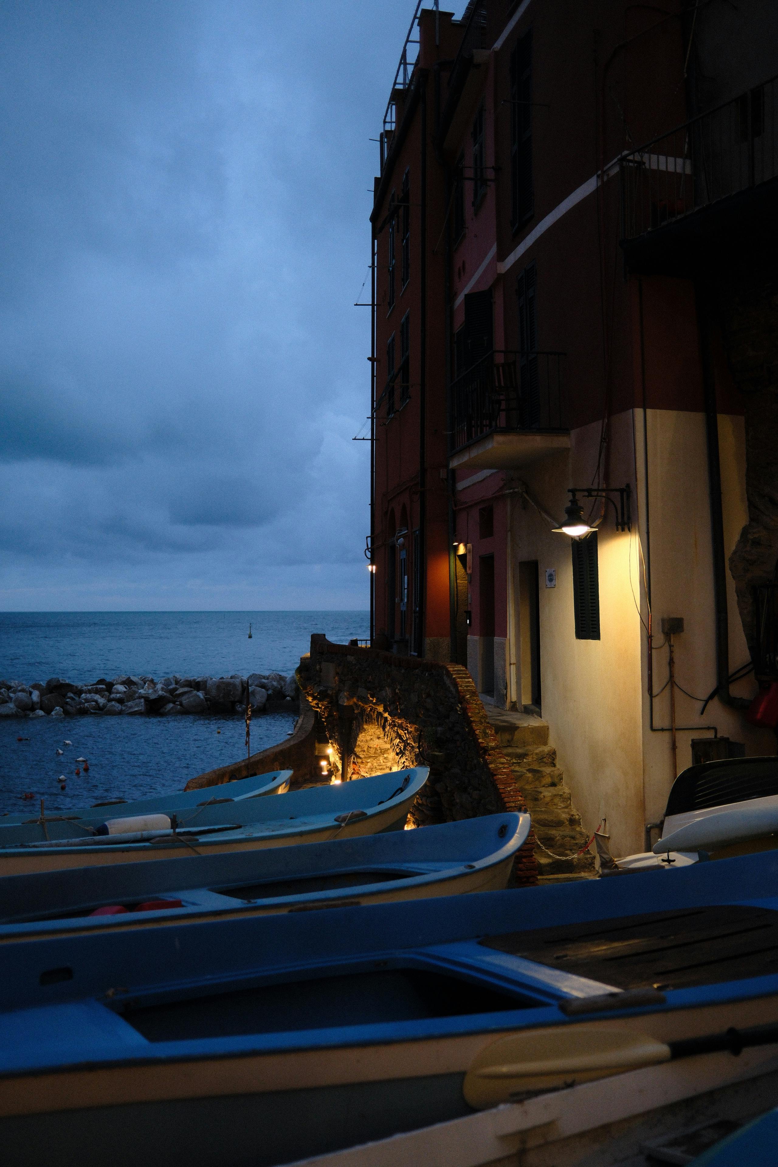 grátis Cena tranquila ao entardecer no porto de Riomaggiore, destacando a arquitetura encantadora e os barcos atracados. Foto profissional