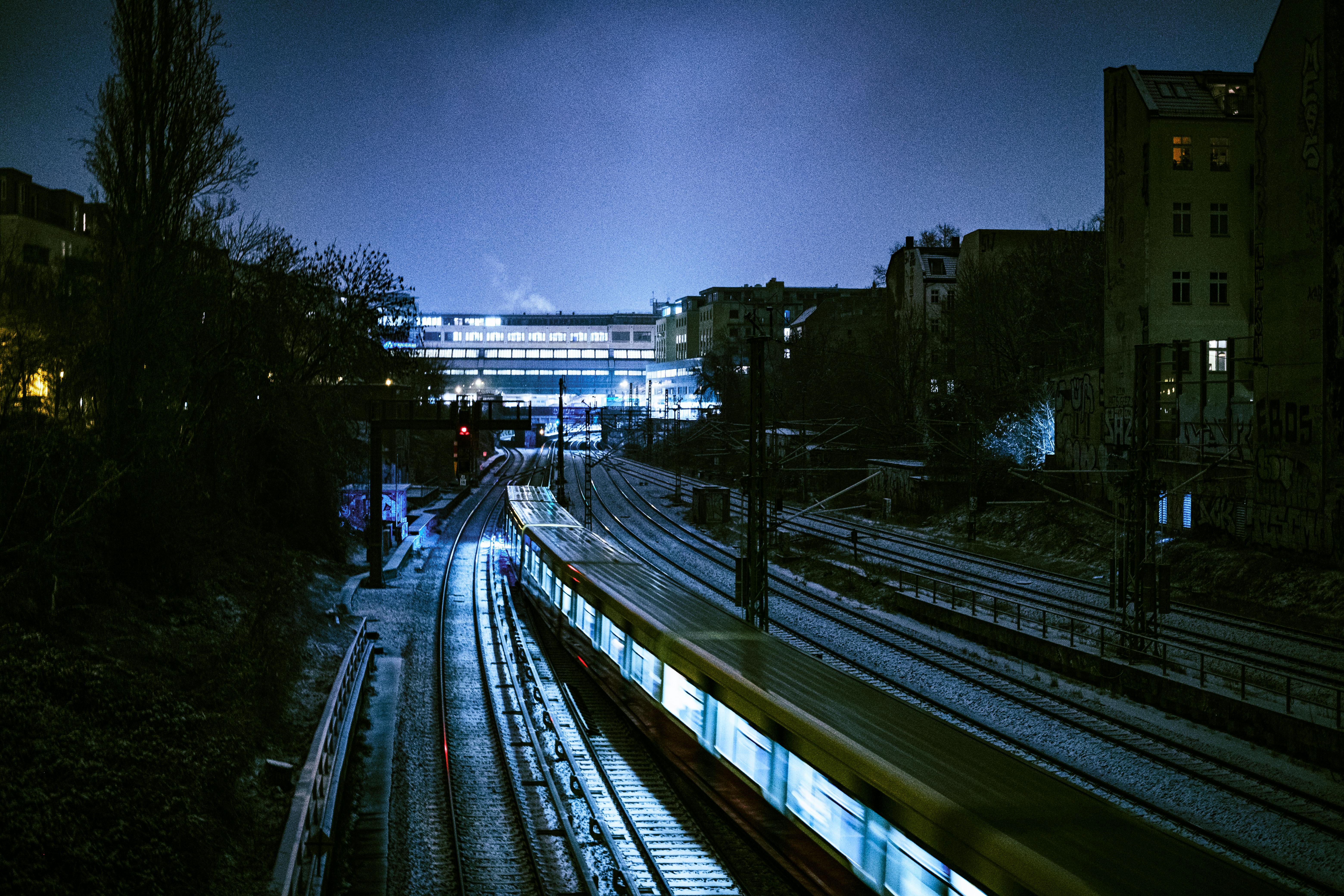 Bezpłatne Nocnym potokiem przez tory w Berlinie przejeżdża pociąg, rozświetlany światłami miasta. Zdjęcie z galerii