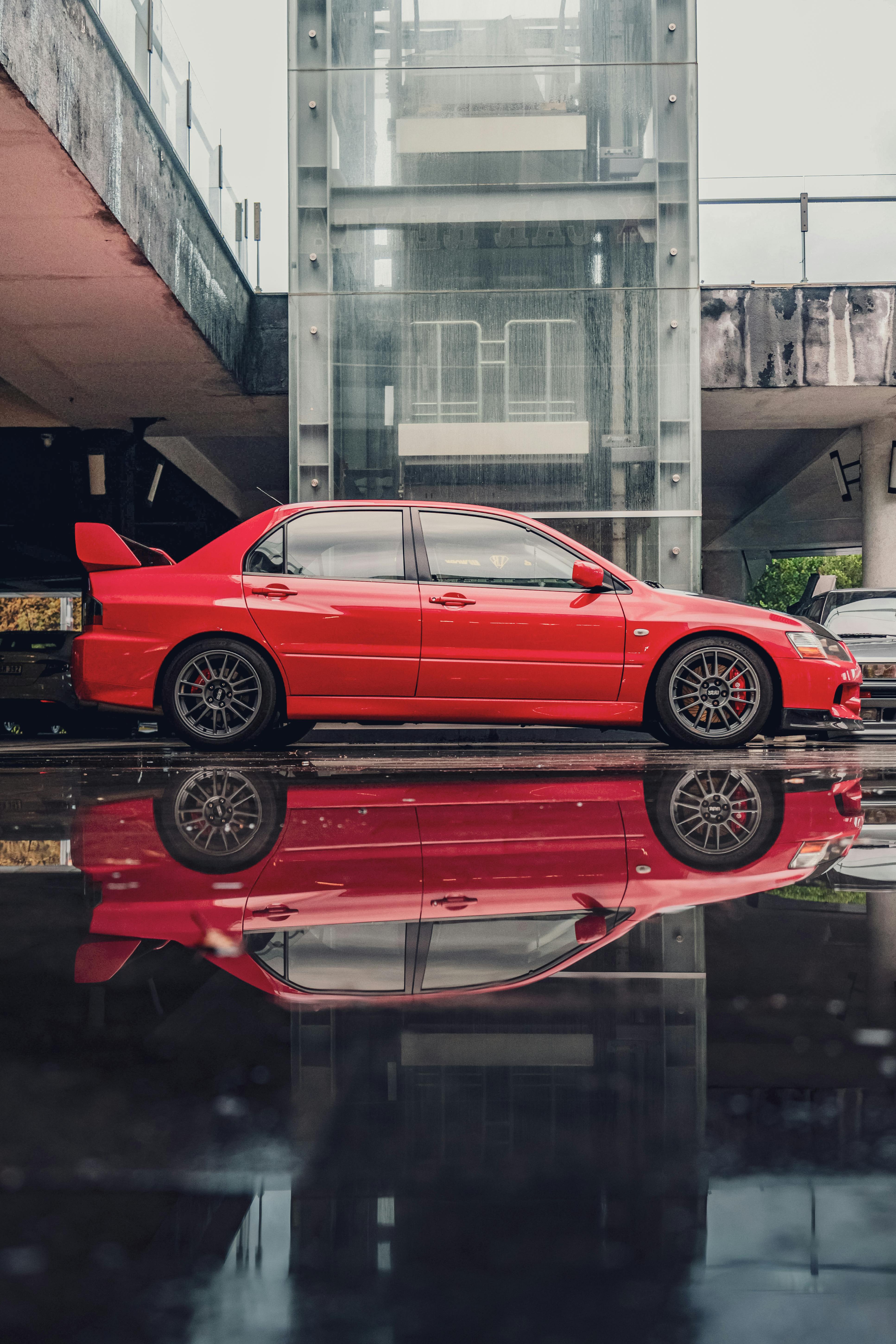 gratis Een rode sportwagen op een regenachtige dag, met zijn weerspiegeling in een plas. Stockfoto