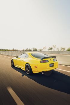 A sleek yellow sports car speeds down a highway under a clear sky.