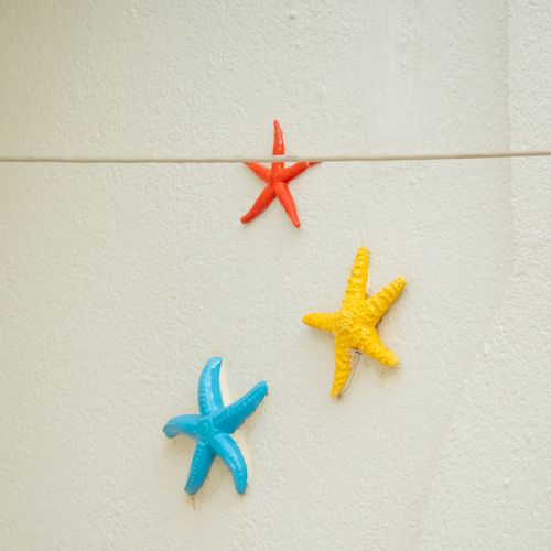 Free Vibrant red, blue, and yellow starfish decorations on a white textured wall, indoor setting. Stock Photo
