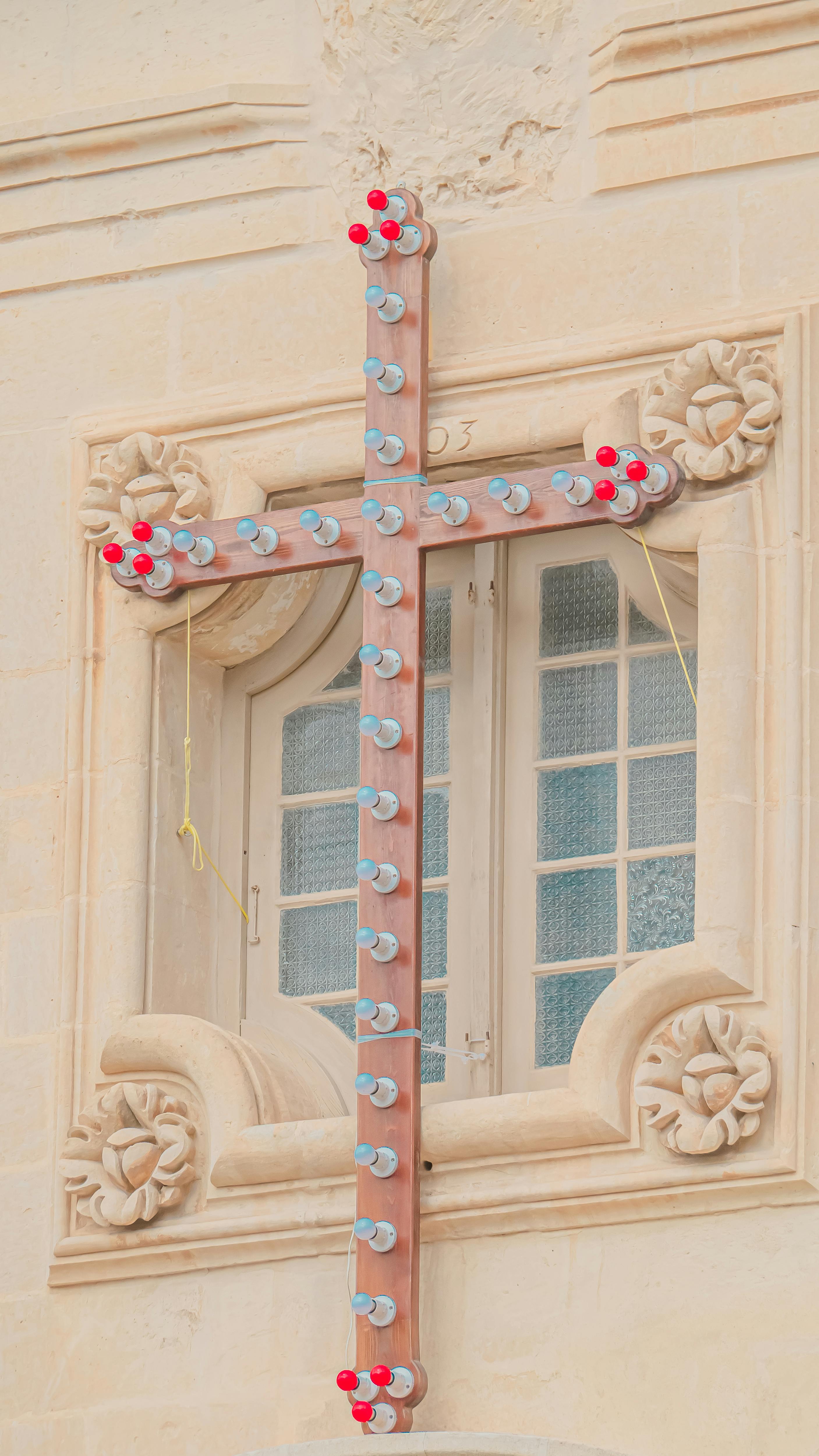 Gratis Una cruz decorativa con bombillas sobre un muro de piedra ornamentado, que realza la arquitectura histórica. Foto de stock