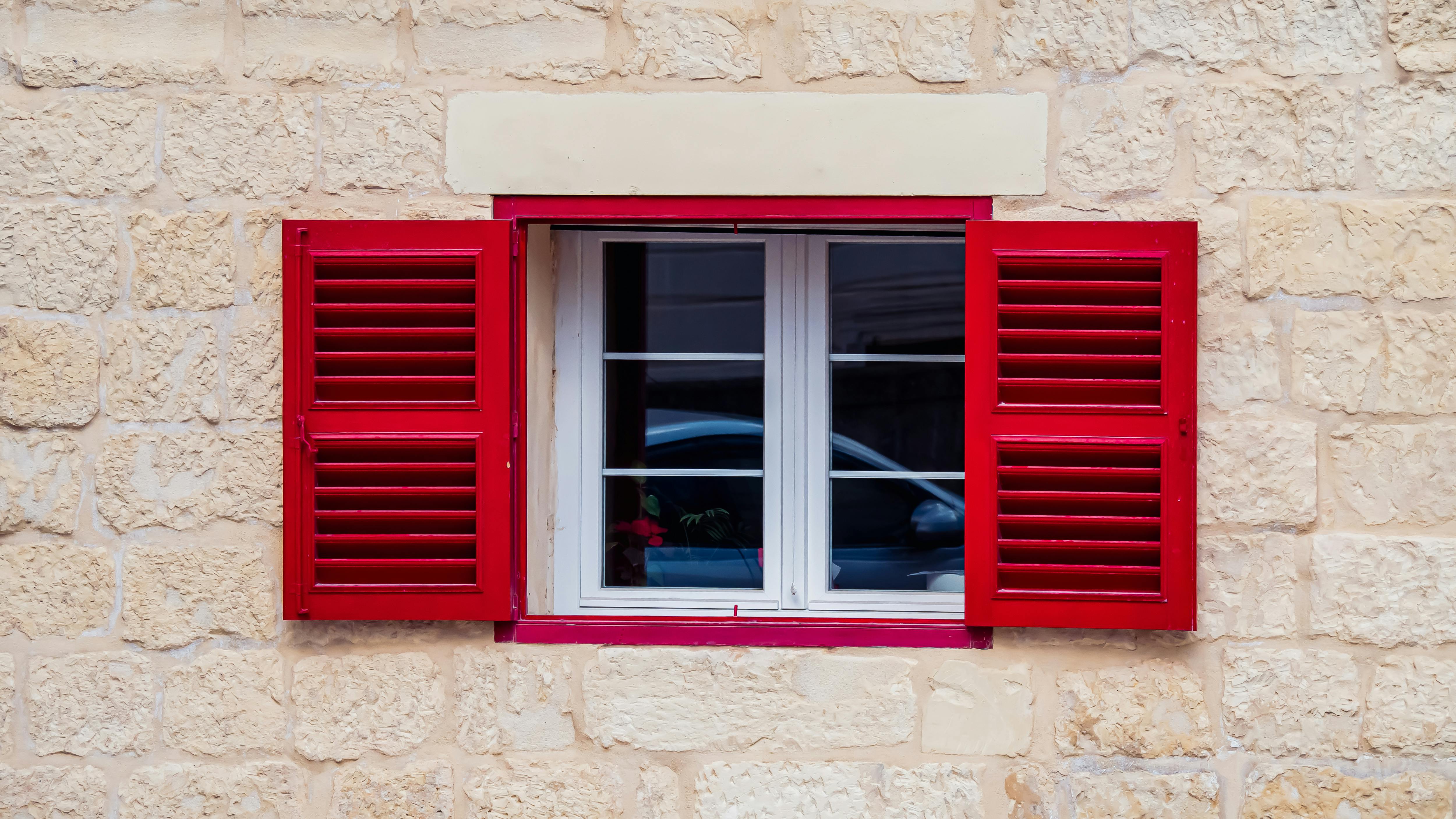 gratis Een raam met rode luiken in een rustieke stenen muur, waarin een auto wordt weerspiegeld, toont de architectonische charme. Stockfoto