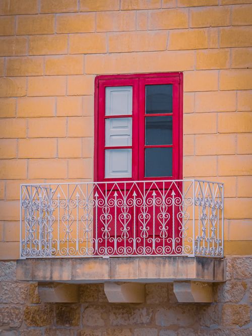 Free Elegant red window with intricate wrought iron balcony against a warm brick wall. Stock Photo