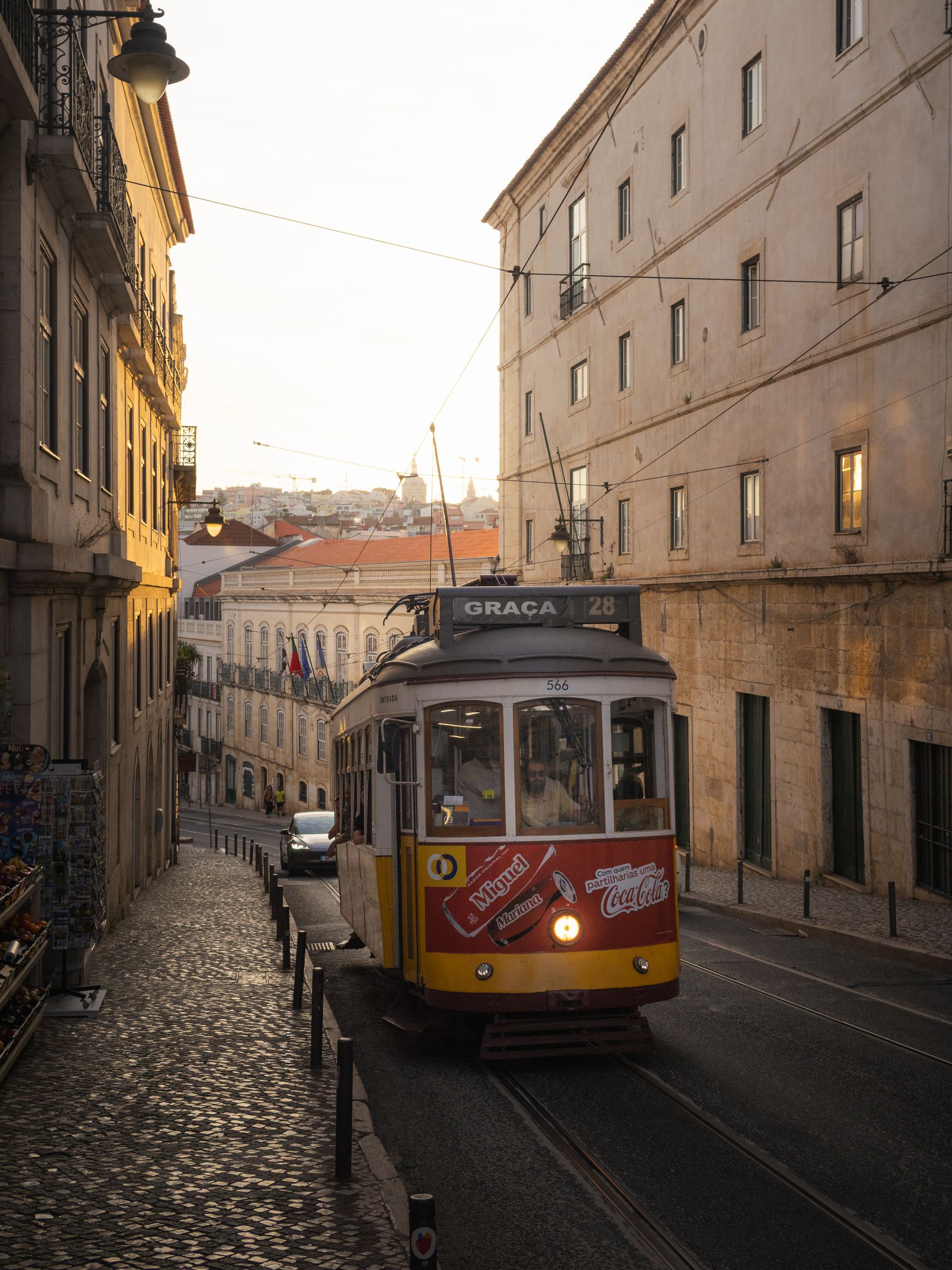 A yellow tram climbing a cobbled street in Lisbon at sunset