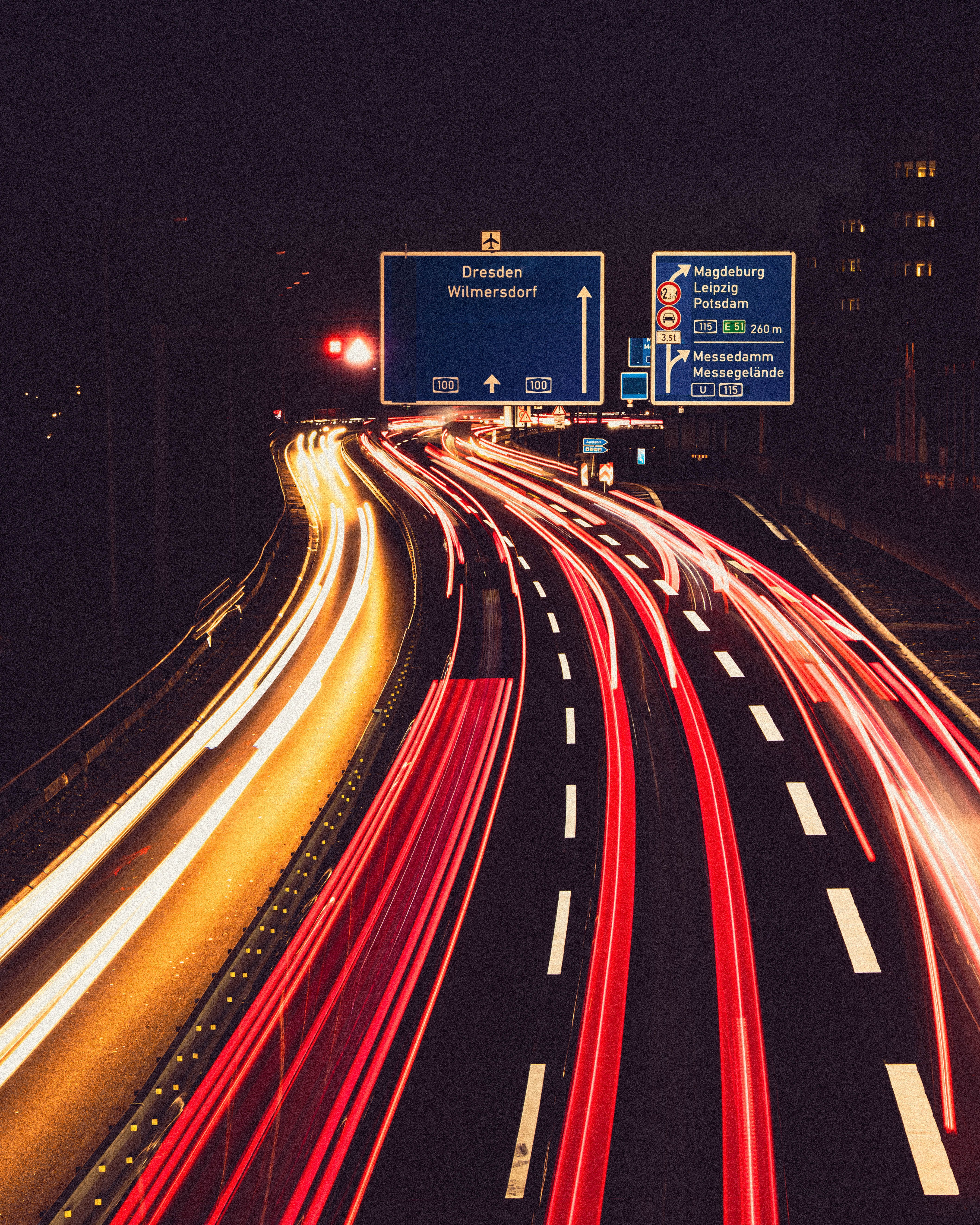 Long exposure of light trails on autobahn with Dresden signage, creating dynamic motion effect at night.