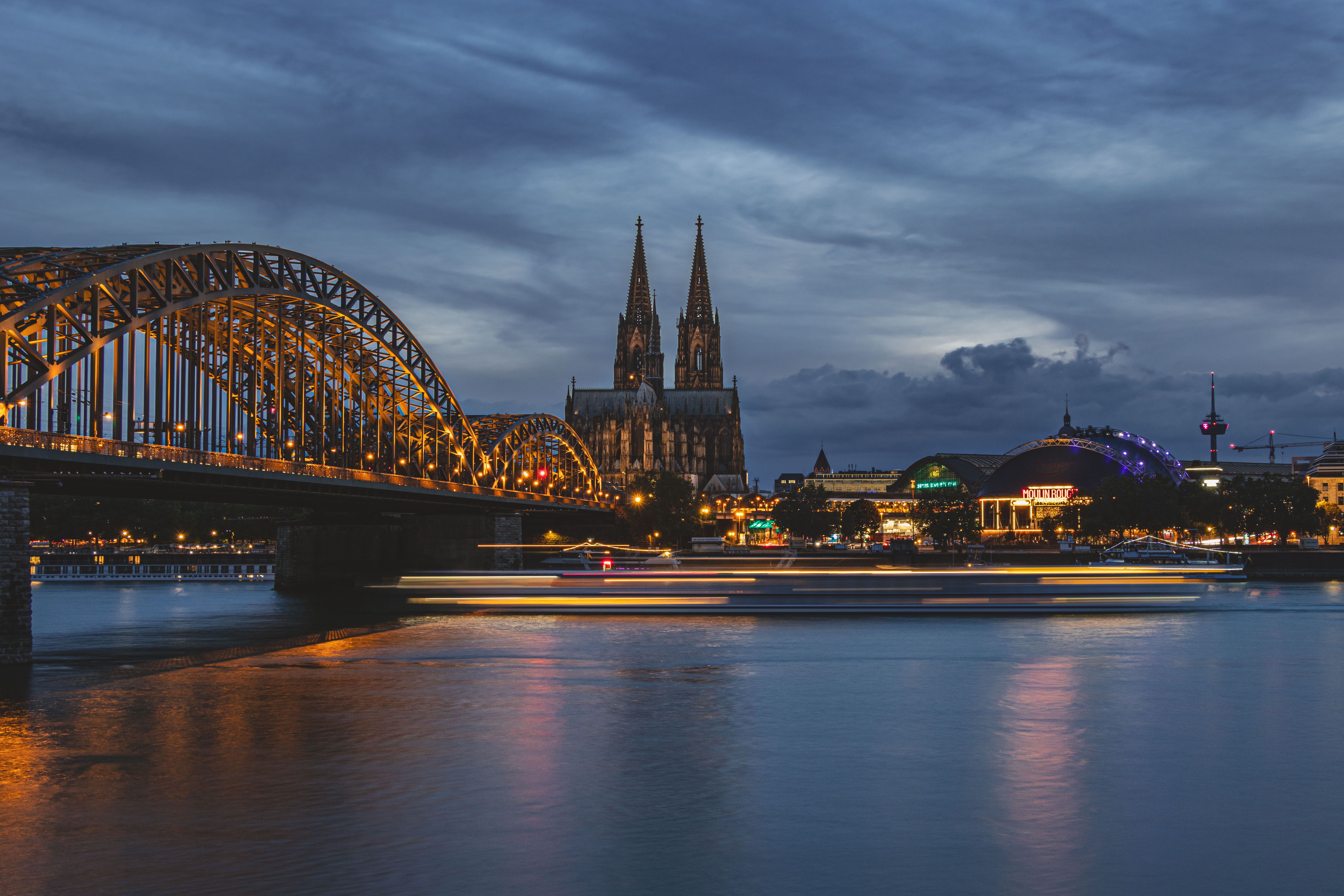 Dramatic view of Cologne Cathedral and Hohenzollern Bridge illuminated at twilight over the Rhine River.