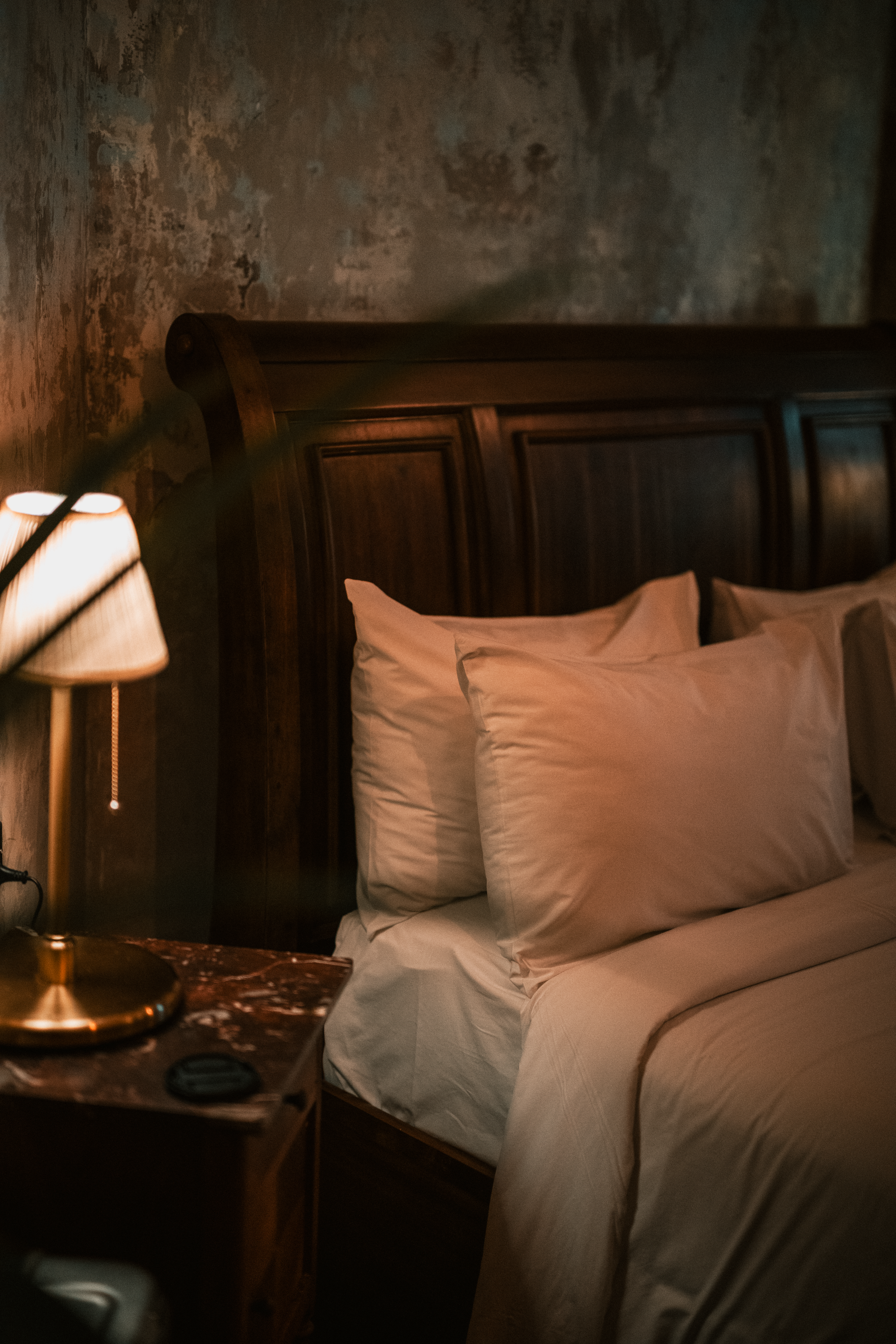 Intimate bedroom with a timber bed, beige curtains and soft amber bedside lighting at night