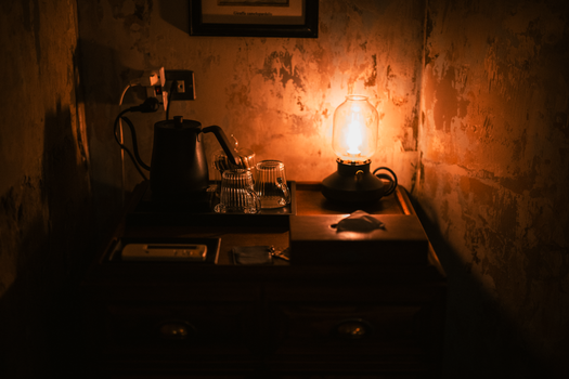 Warm, cozy corner of a room with a vintage lamp illuminating glassware on a wooden surface.
