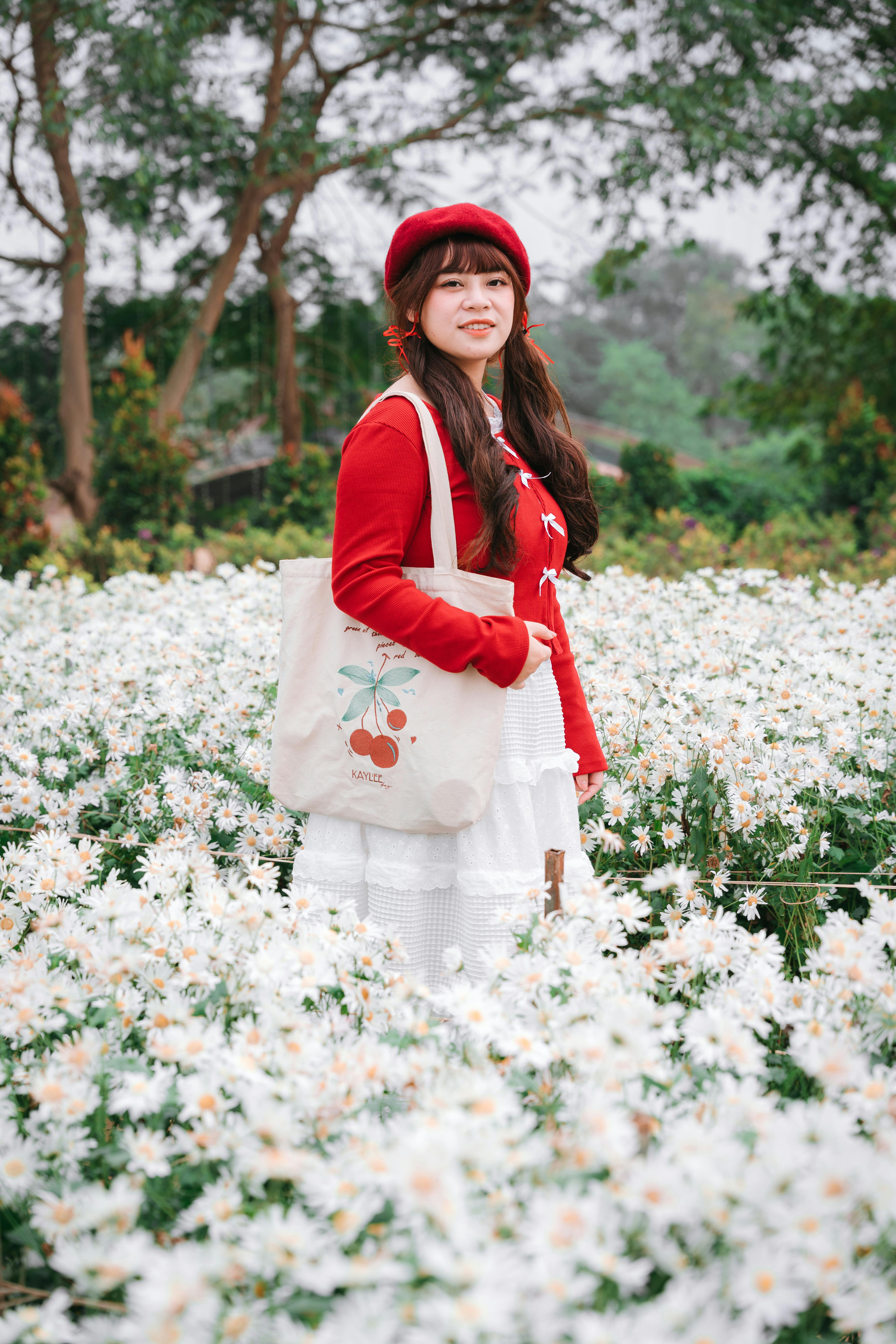 bezplatná Mladá žena v červeném oblečení stojící v květinové zahradě v Hanoji, obklopená bílými květy. Základová fotografie