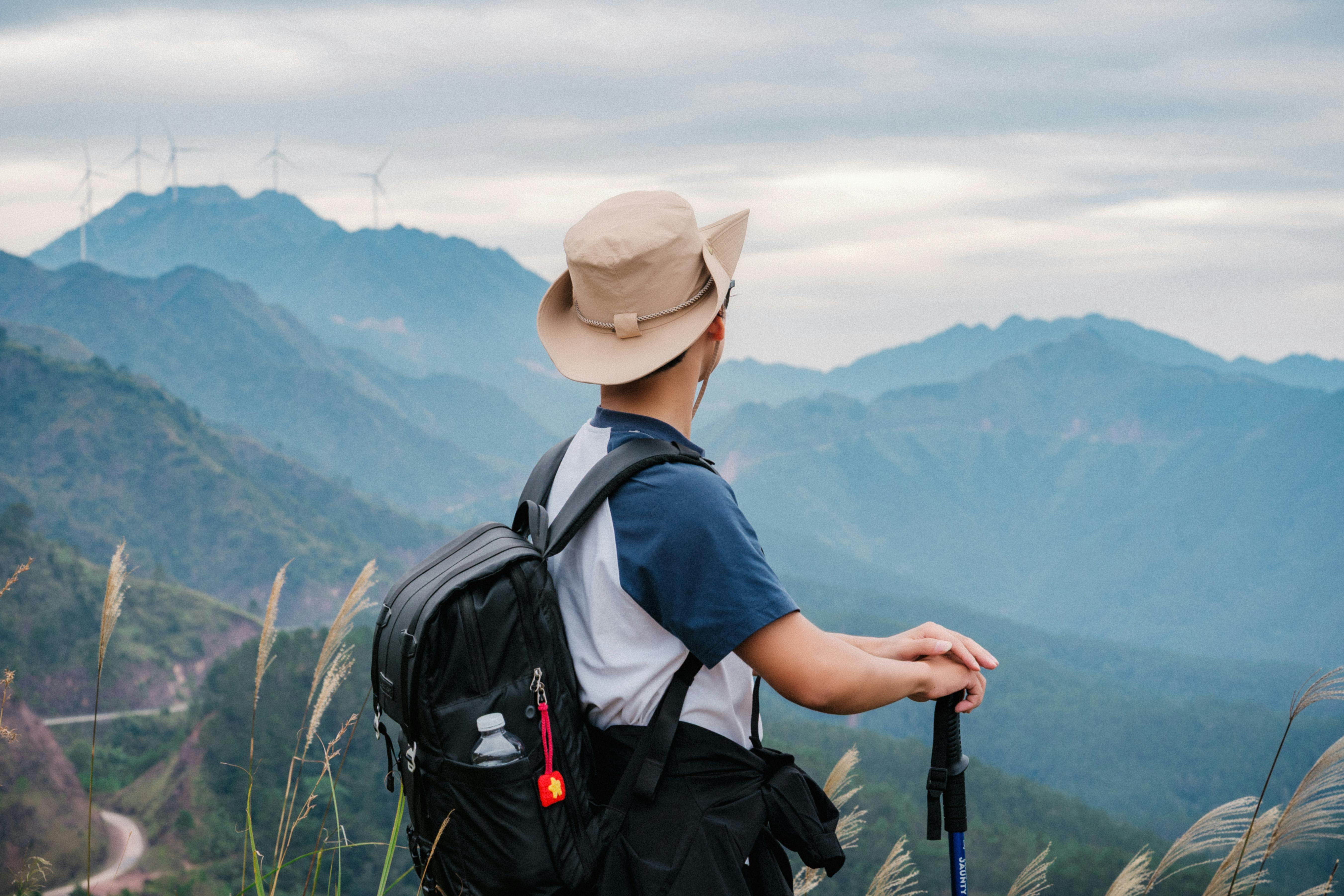 bezplatná Dobrodružný turista s batohem obdivuje během dne větrné turbíny a hory v Quảng Ninh ve Vietnamu. Základová fotografie