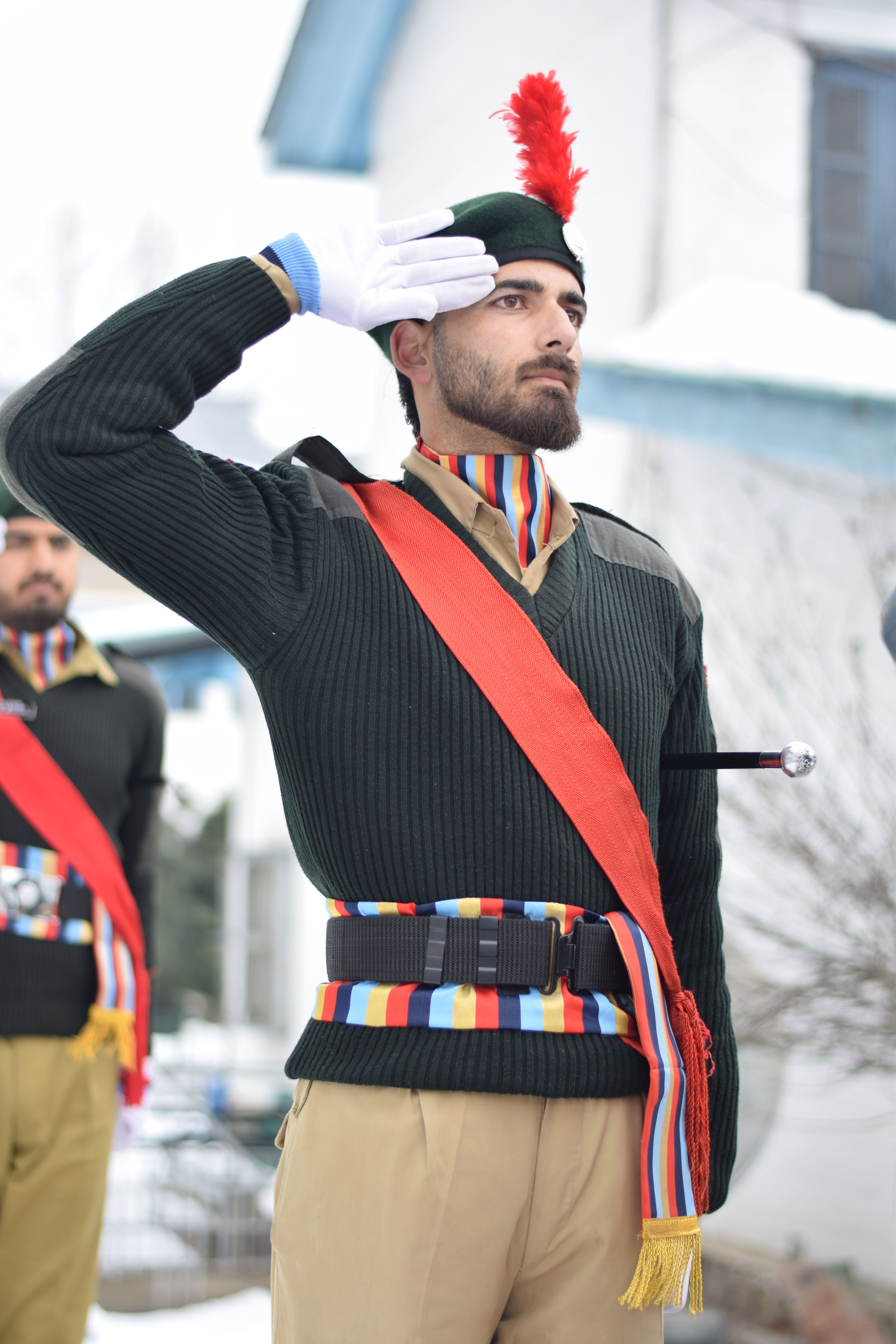 Close-up of a male soldier saluting outdoors, wearing a colorful uniform in a snowy setting.