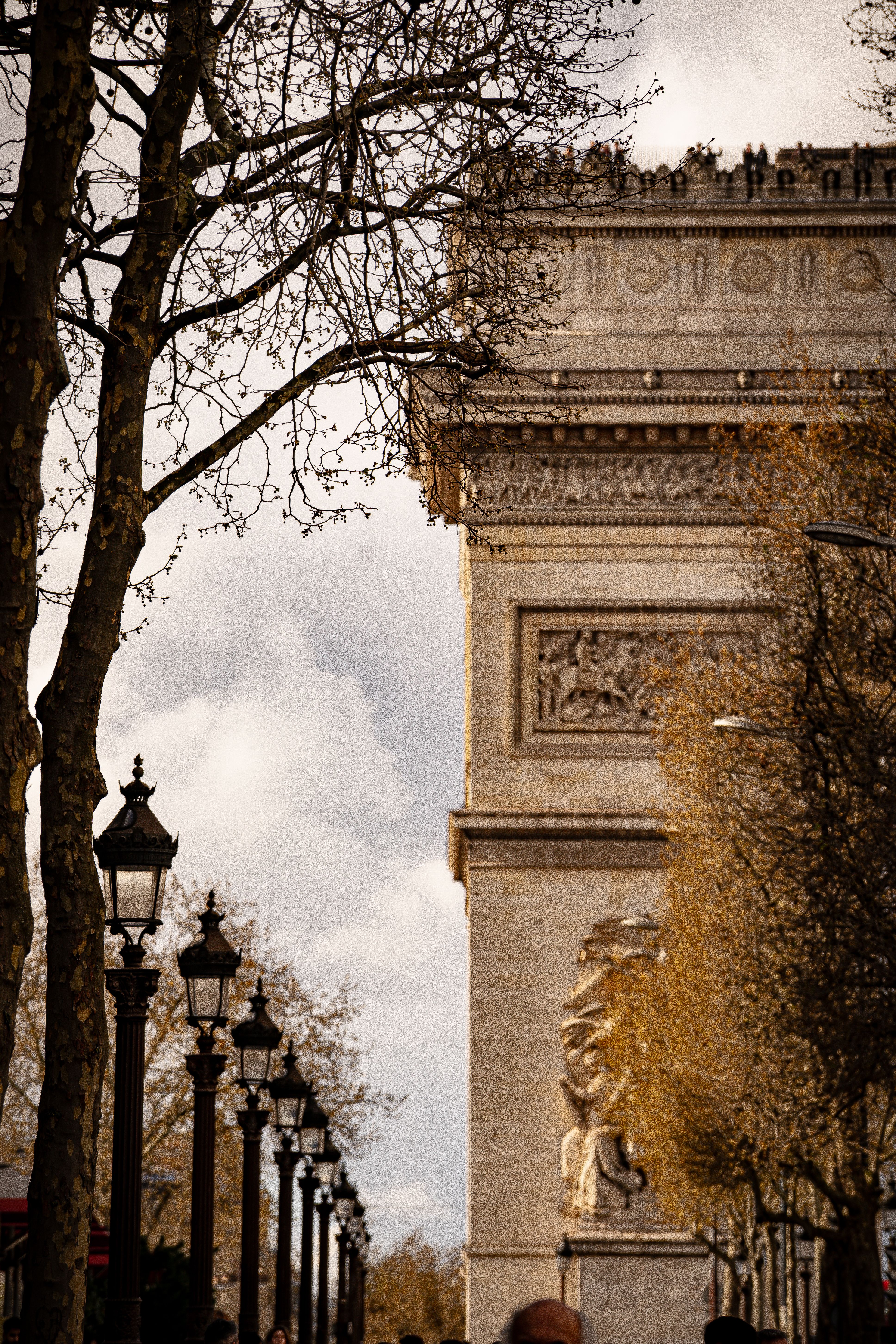 A stunning view of the Arc de Triomphe in spring, framed by trees and lampposts along a Paris street.
