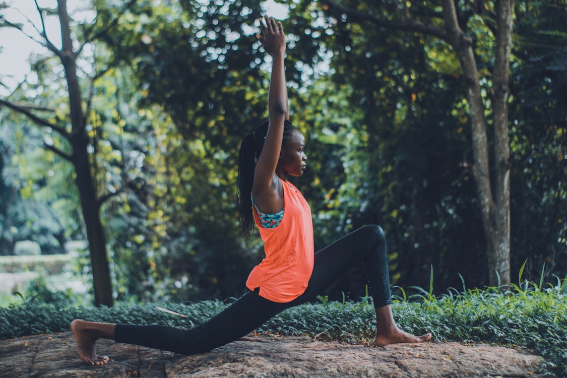 Free Photo of Woman in Orange Tank Top and Black Pants Striking a Yoga Pose Outdoors Stock Photo