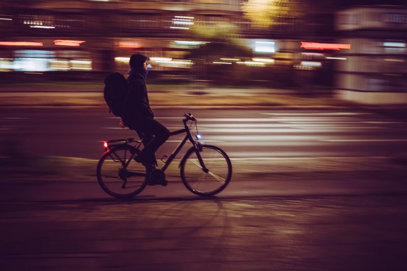 Blurry image of a cyclist moving swiftly through illuminated city streets at night.